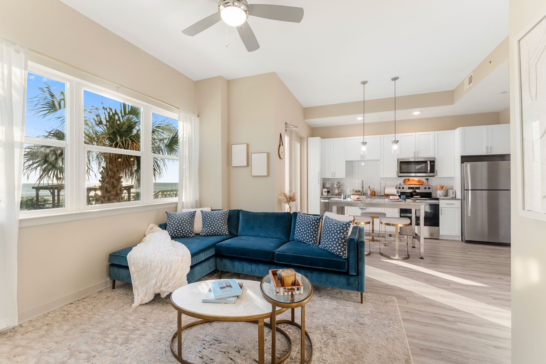 Bright apartment living area featuring a chic blue sectional, elegant decor, and a modern open kitchen with stainless steel appliances.