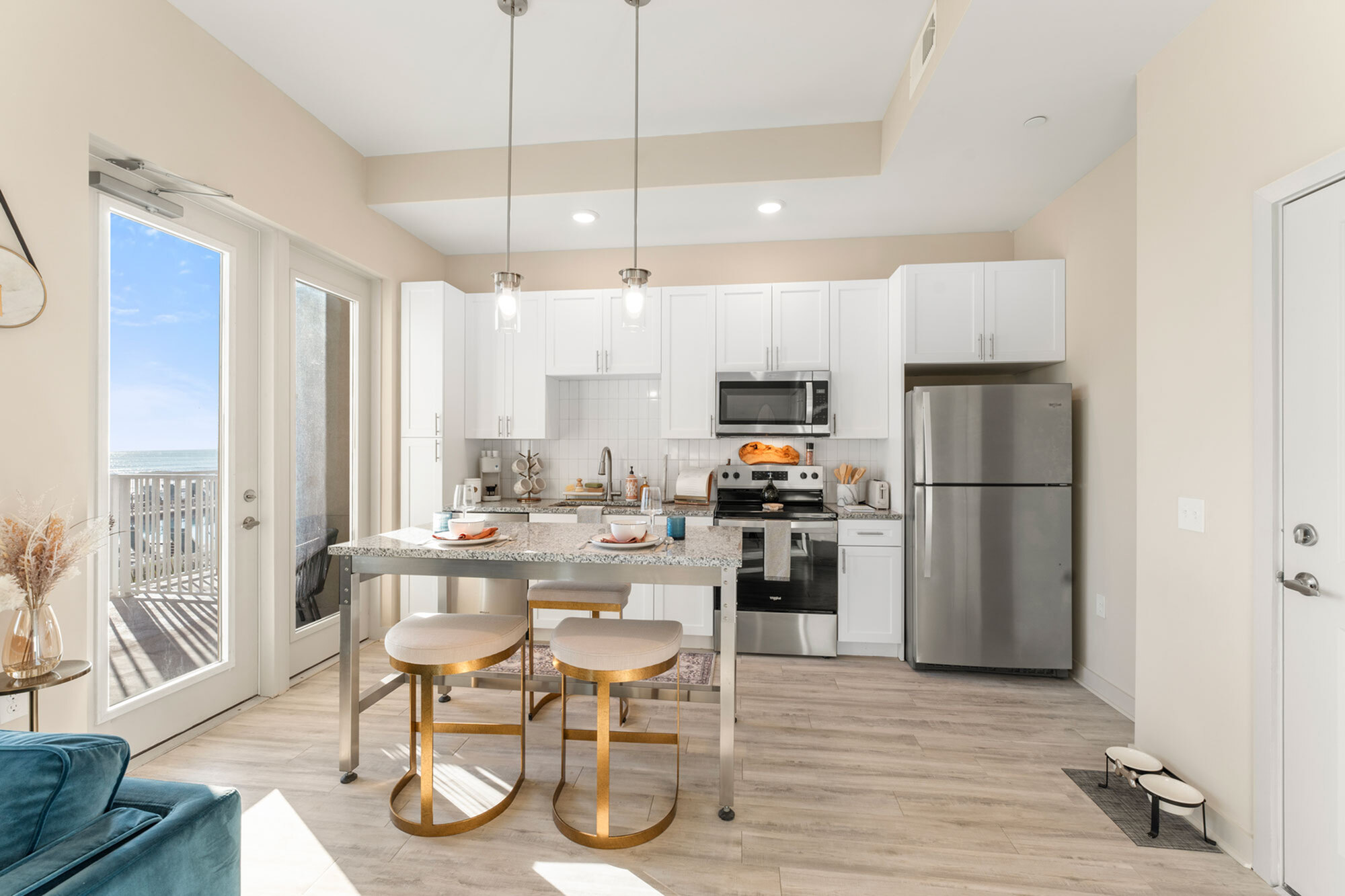 Contemporary kitchen with sleek stainless steel appliances, chic pendant lighting, and dining seating overlooking a sunlit balcony.