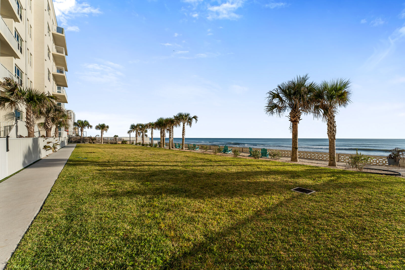 Oceanfront apartment view featuring a lush, sunlit lawn with palm trees and a serene beach, perfect for coastal living.