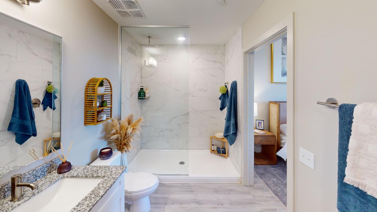 Modern bathroom featuring a sleek walk-in shower, elegant marble wall tiles, and stylish decorative accents including plants and navy towels.