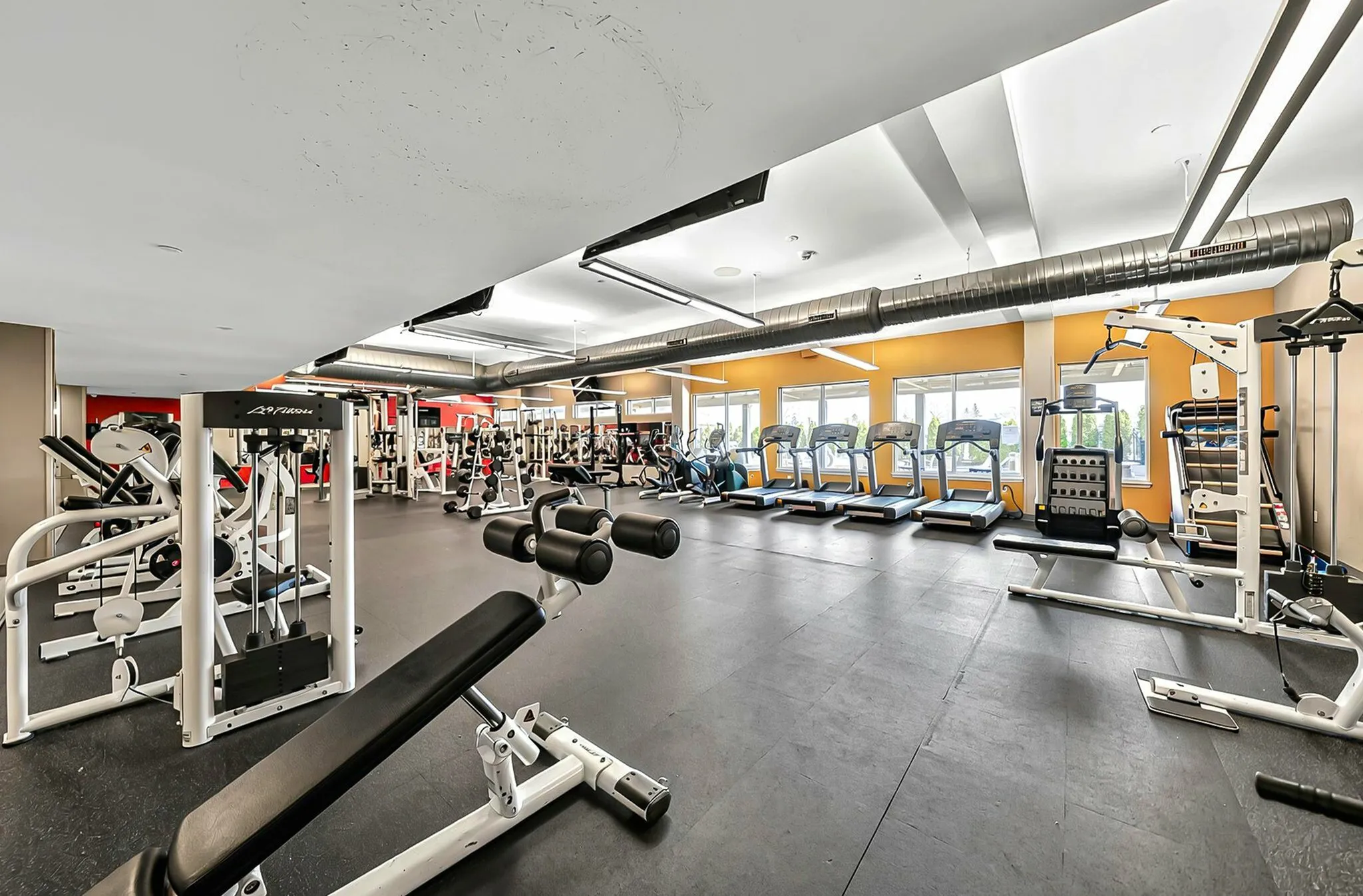 Expansive fitness center with modern exercise equipment, sleek treadmills, bright windows, and spacious workout areas for an invigorating gym experience.