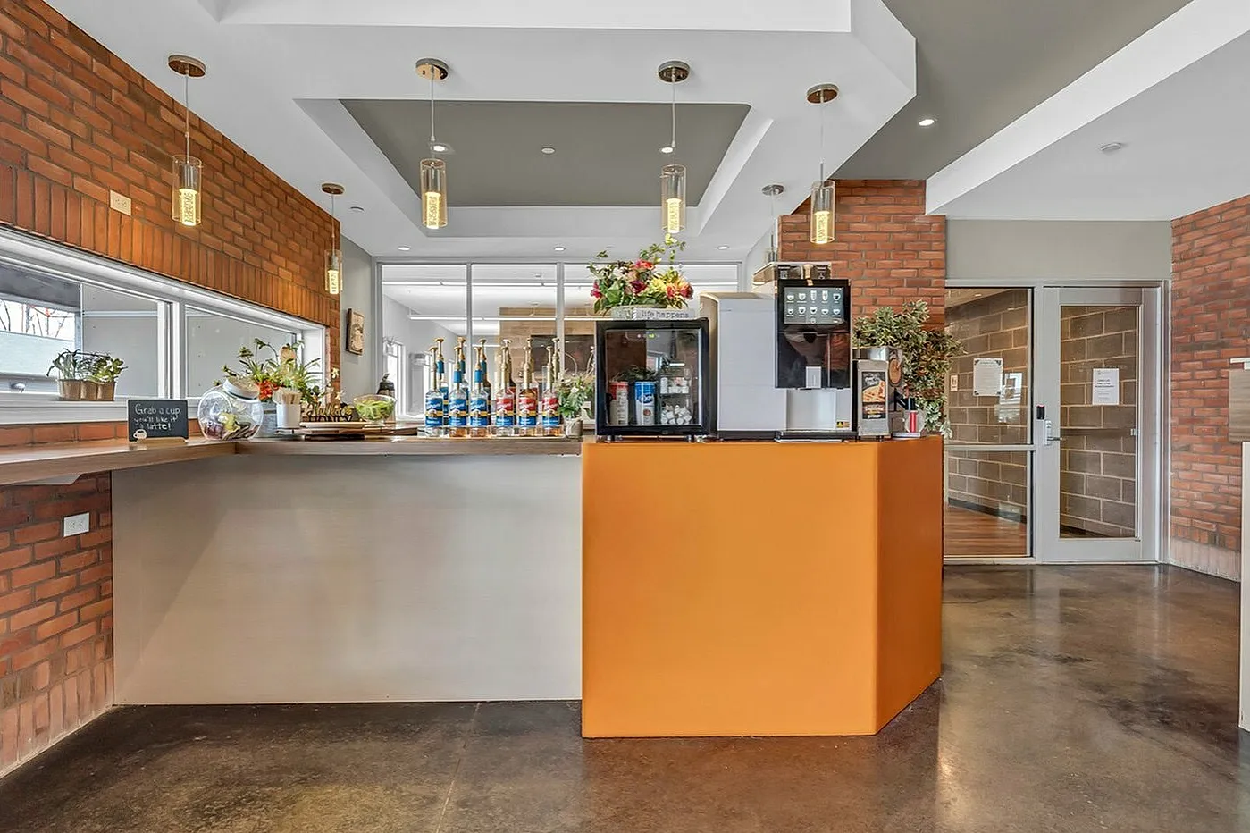 Chic and contemporary cafe with brick walls, warm lighting, and a vibrant orange counter offering a welcoming atmosphere.