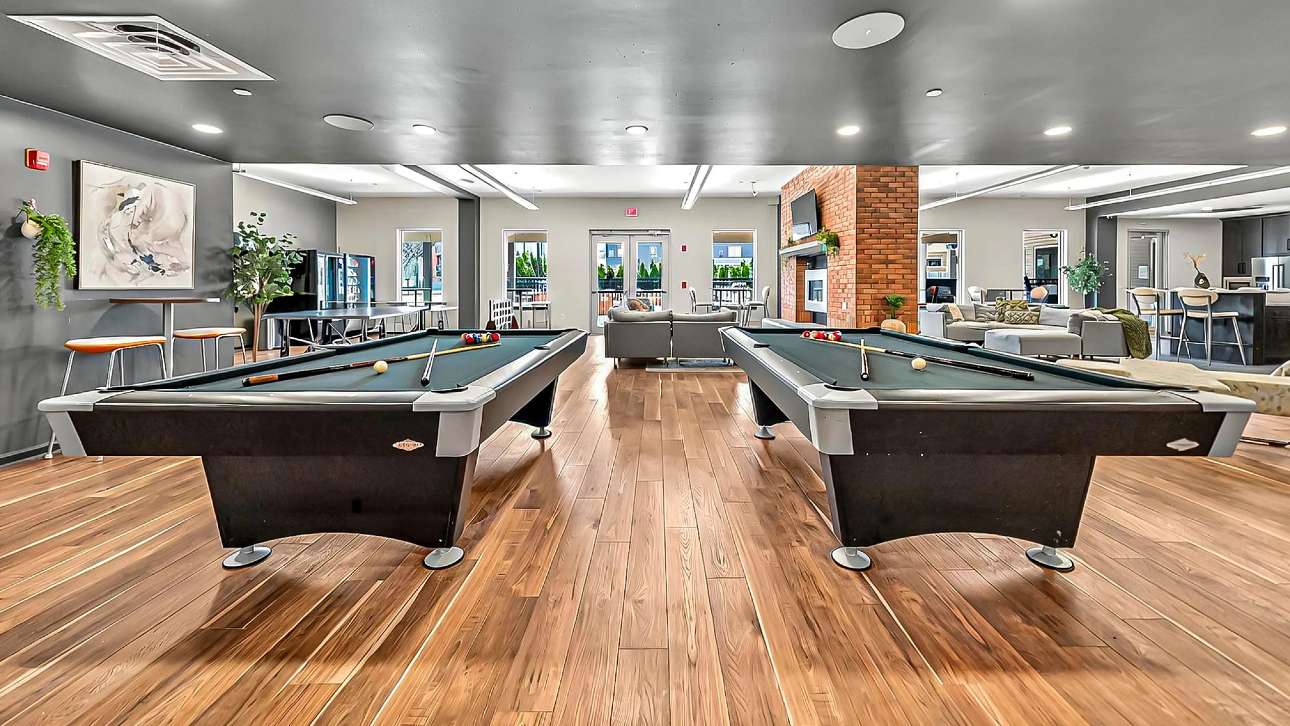 Luxe community game room with sleek pool tables, modern seating, and a cozy brick fireplace, ideal for social gatherings.