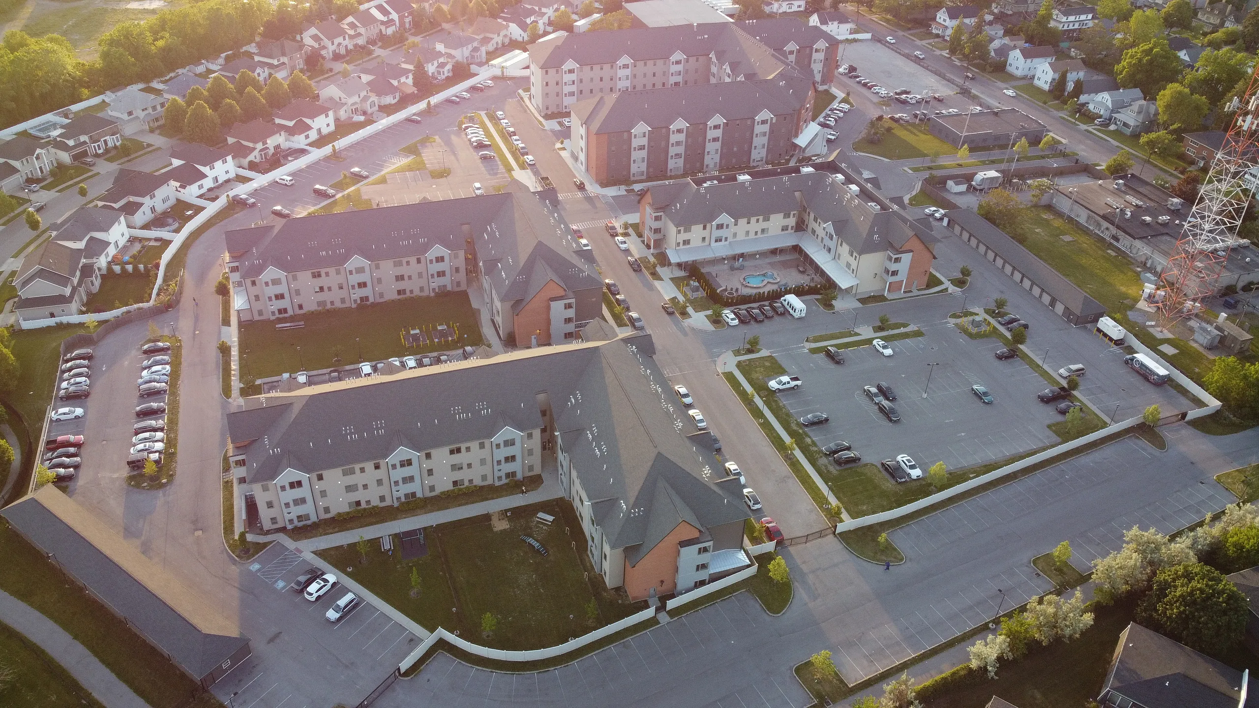 Aerial view of a modern apartment complex featuring spacious parking areas, lush green surroundings, and stylish architecture, perfect for comfortable living.