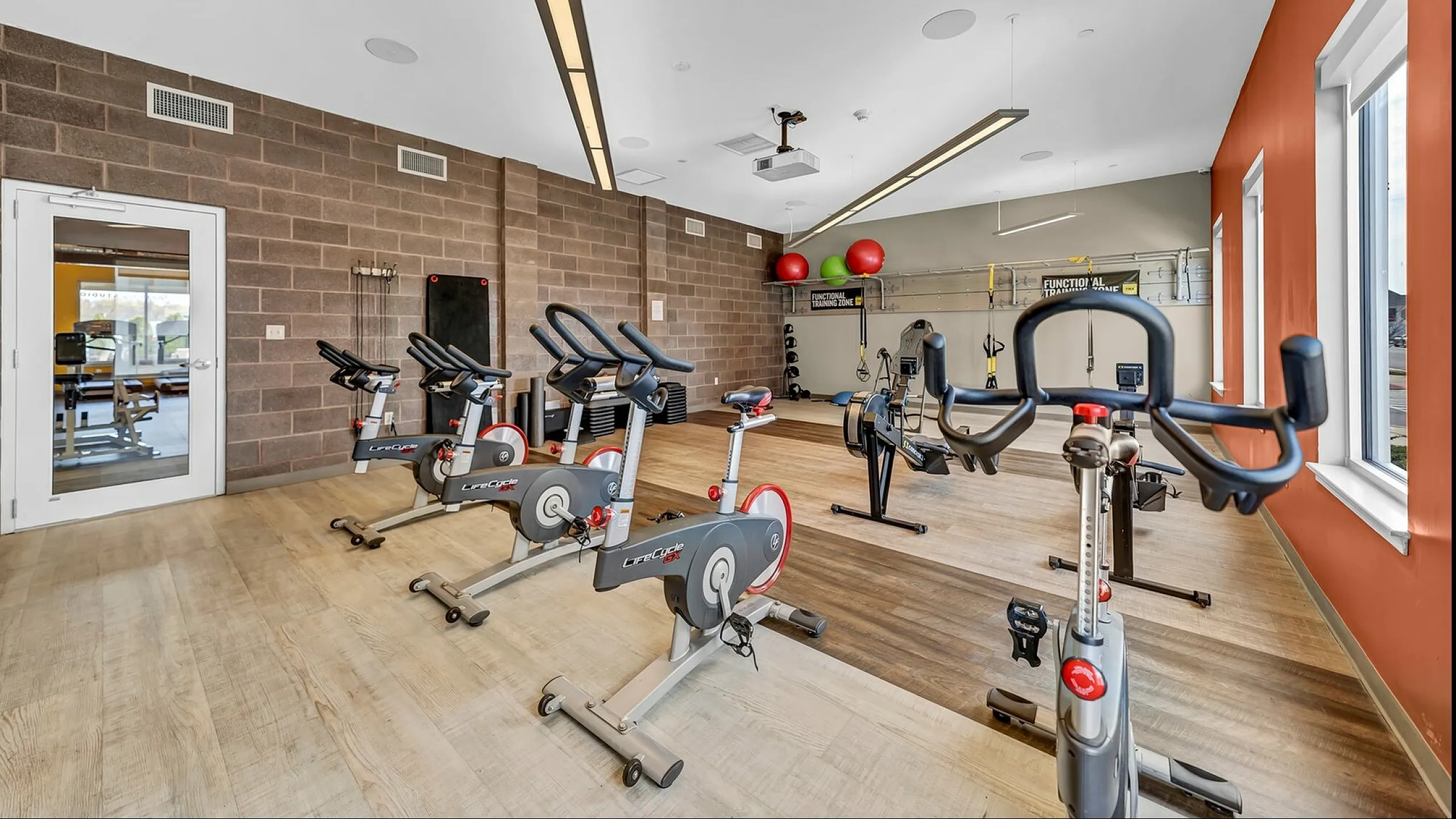 Modern fitness room with state-of-the-art exercise bikes and functional training equipment, featuring large windows and vibrant decor.