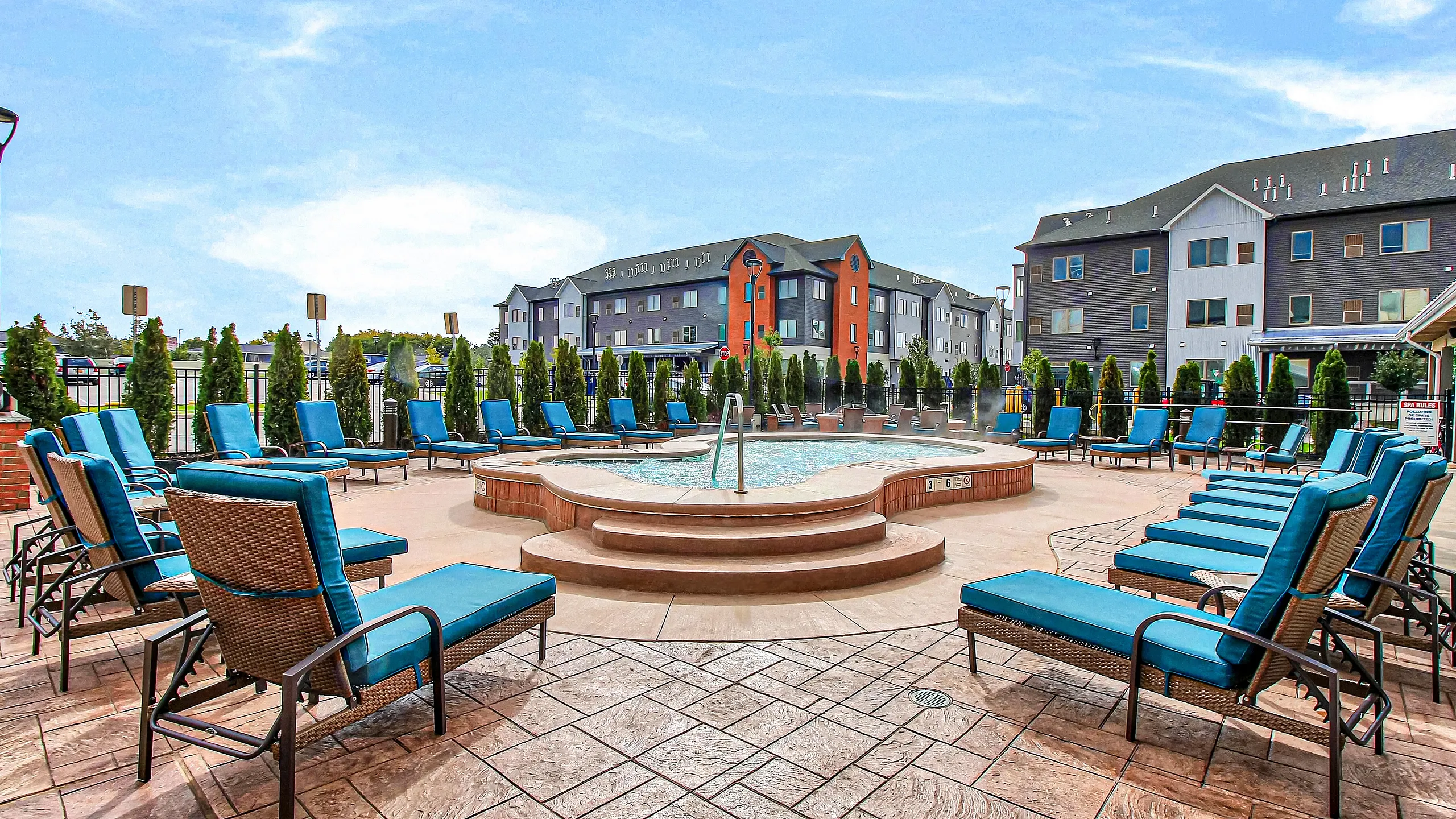 Luxurious outdoor pool area featuring stylish lounge chairs under a bright blue sky, surrounded by modern apartment buildings.
