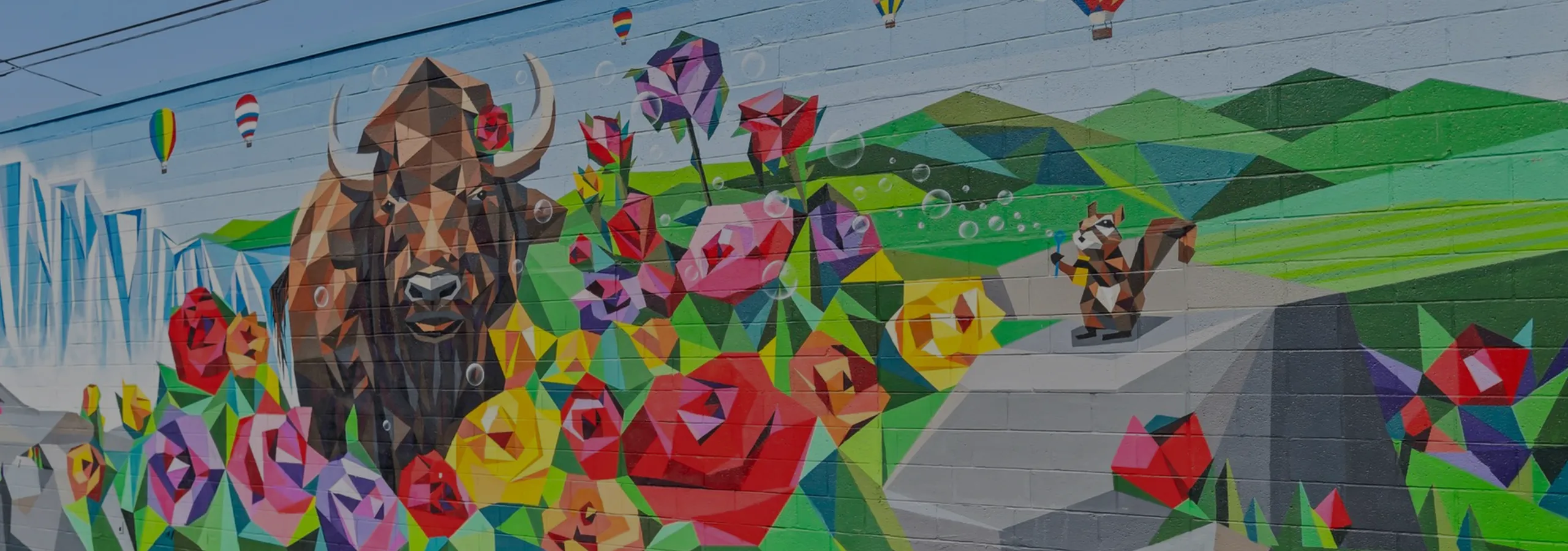 Vibrant mural featuring geometric wildlife with a colorful bison, surrounded by abstract flowers and playful hot air balloons.