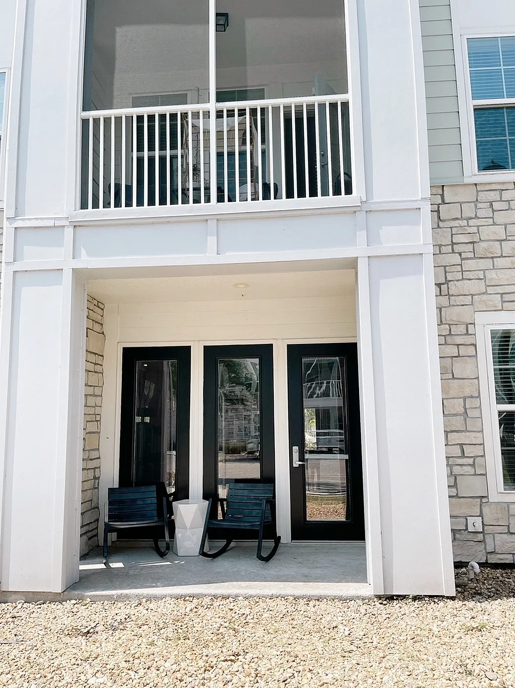 Charming patio with modern rocking chairs in front of elegant double doors, accented by stylish stone wall and large windows.