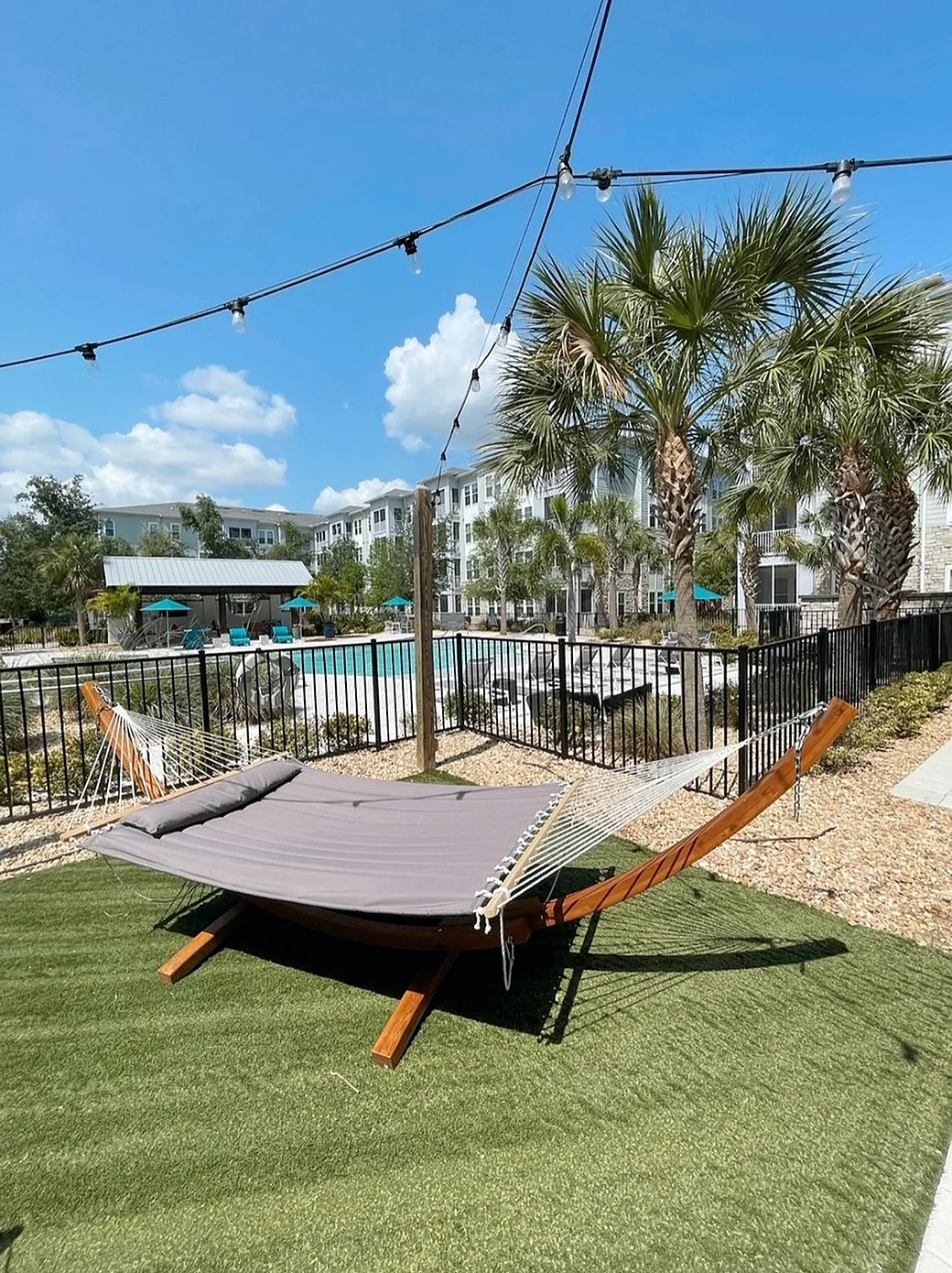 Inviting outdoor oasis with a cozy hammock, vibrant palm trees, and a shimmering pool under clear blue skies.