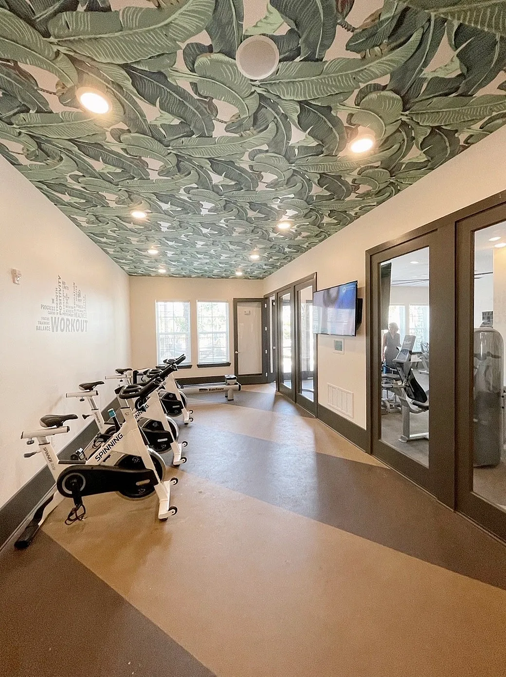 Chic indoor exercise room featuring modern spin bikes and a vibrant tropical ceiling design.