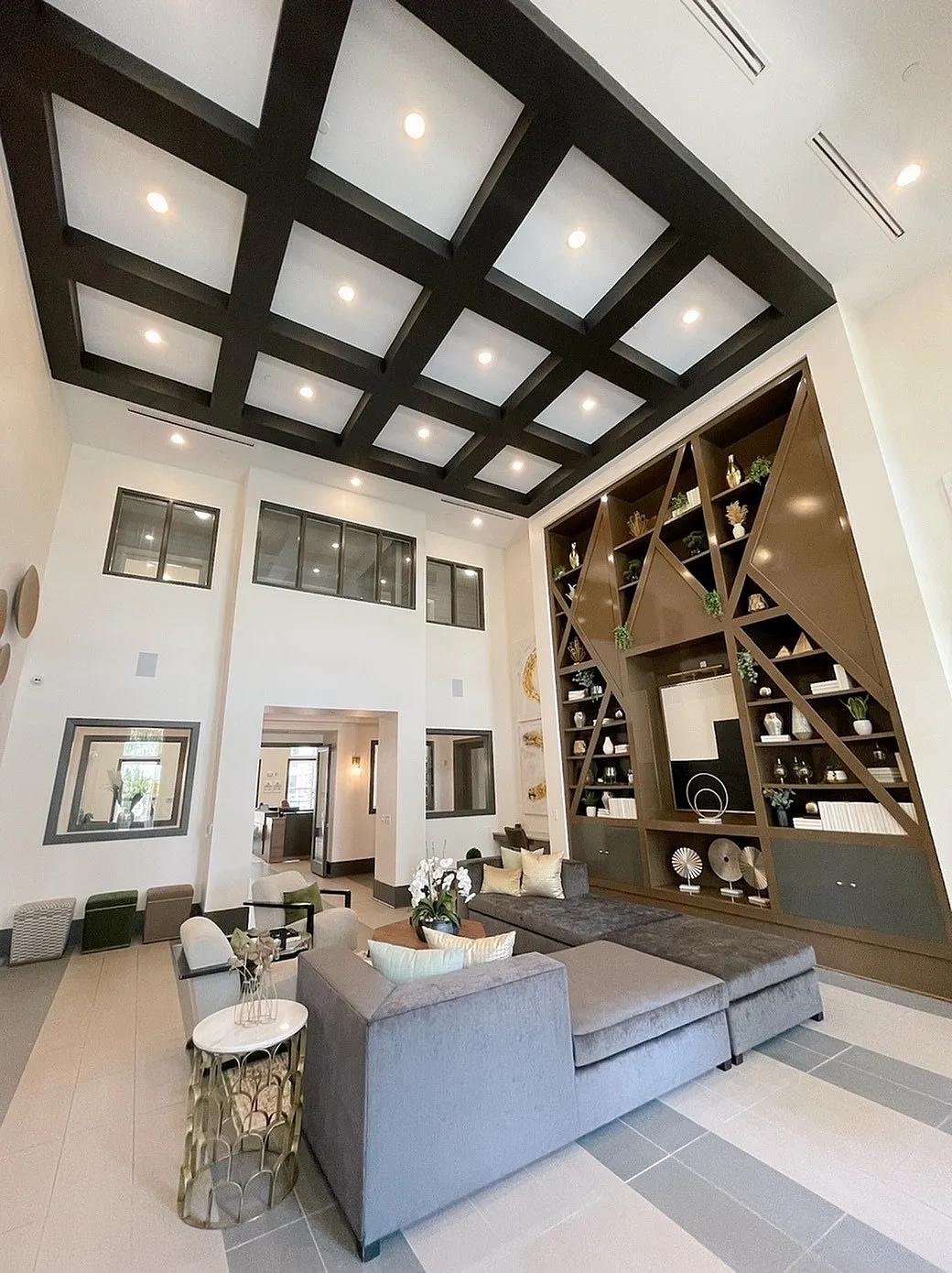 Sophisticated apartment lobby featuring high ceilings, modern geometric shelving, and elegant seating area with plush grey sofas.
