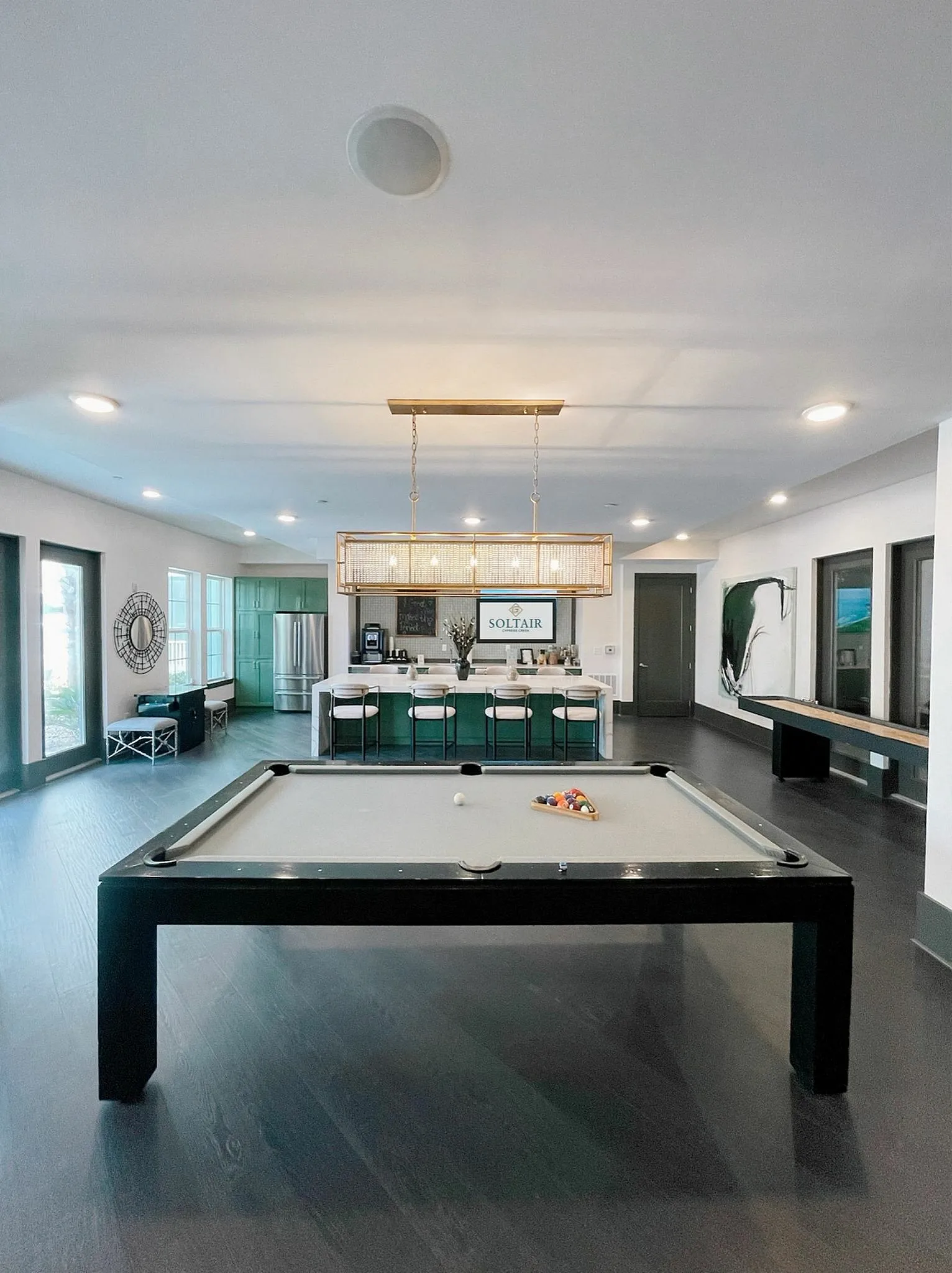 Elegant recreation room featuring a pool table, modern lighting fixture, and open-concept kitchen with bar seating, designed for entertainment and relaxation.