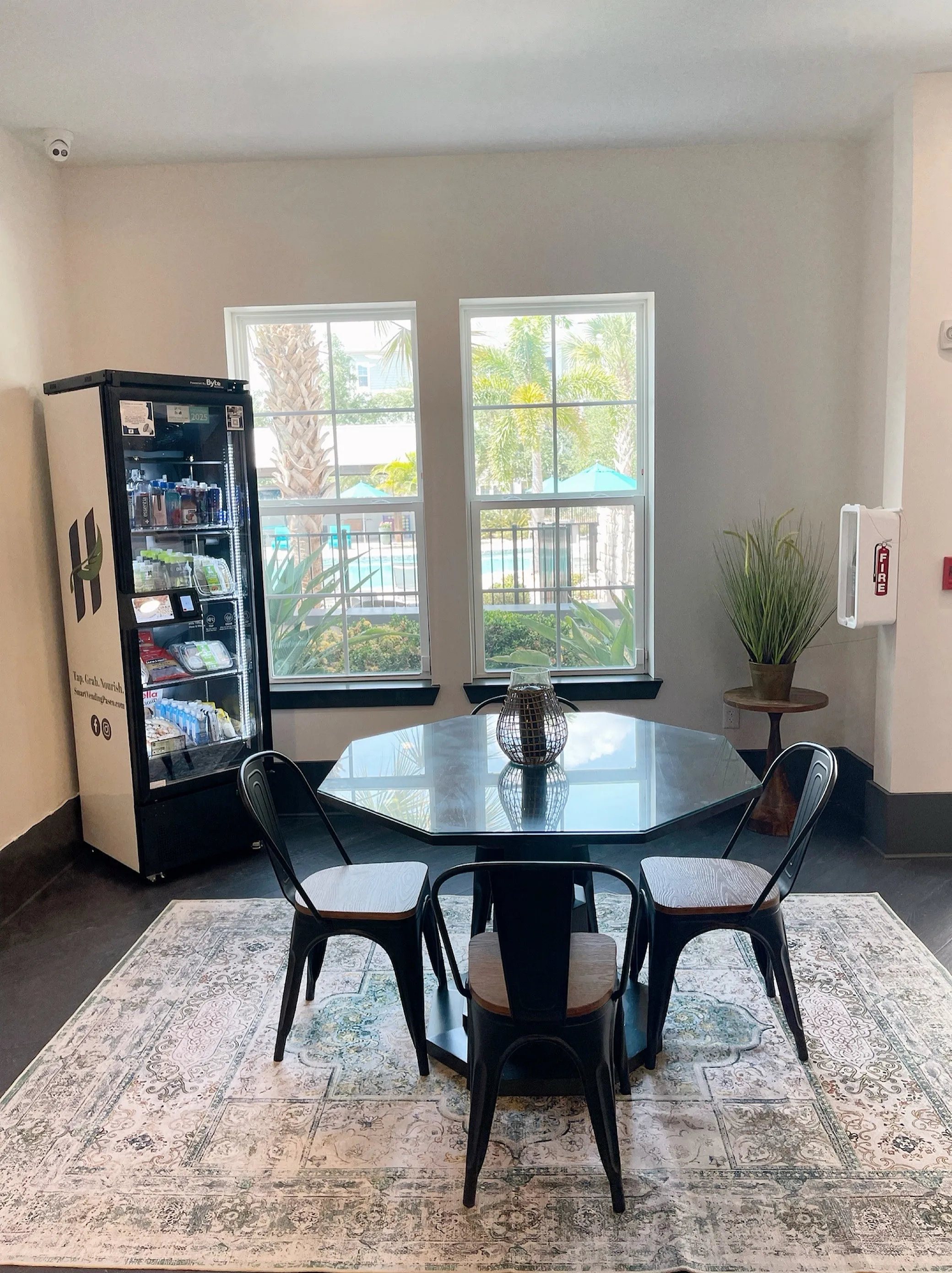 Charming indoor dining area with a modern black table, stylish chairs, and large windows offering a refreshing poolside view.