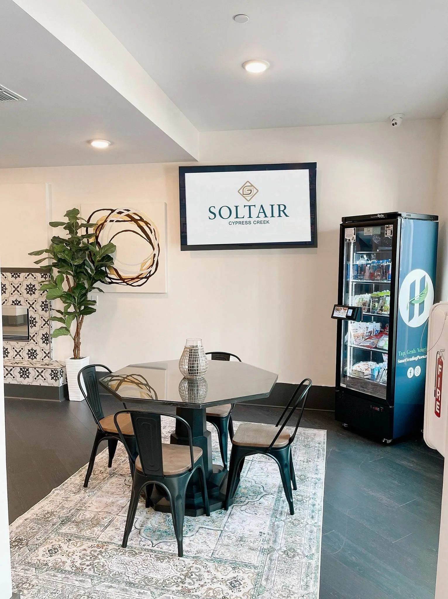 Chic lounge area at Soltair Cypress Creek featuring modern decor, a sleek dining table, vibrant art, and a convenient snack vending machine.