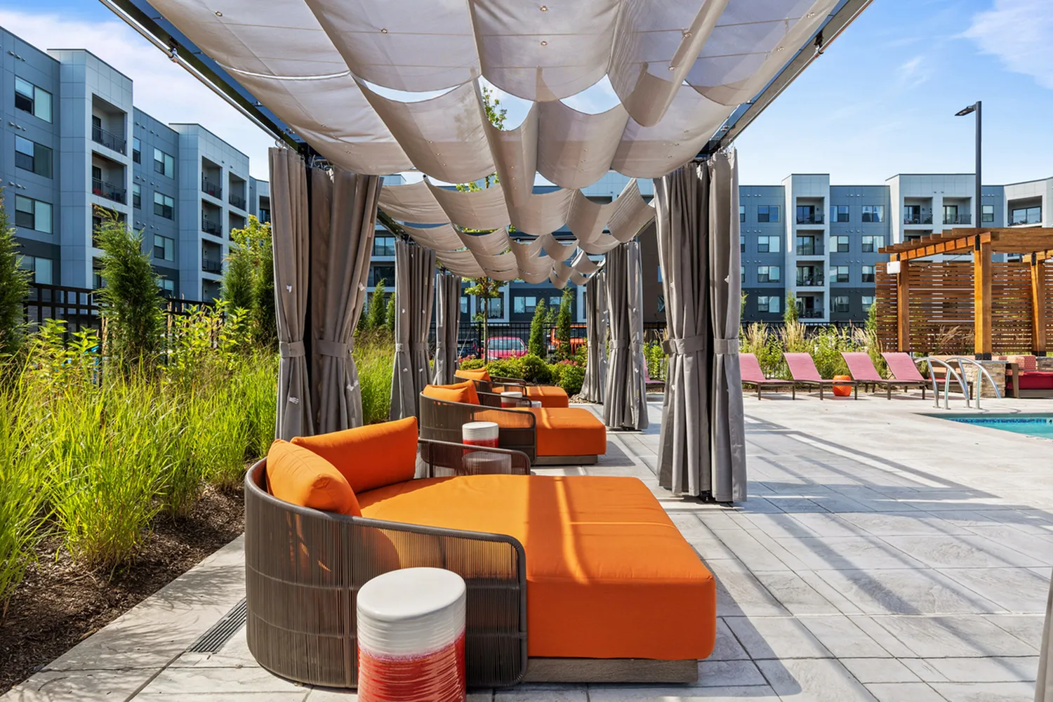 Modern outdoor lounge area with vibrant orange seating under elegant canopy, surrounded by lush greenery.