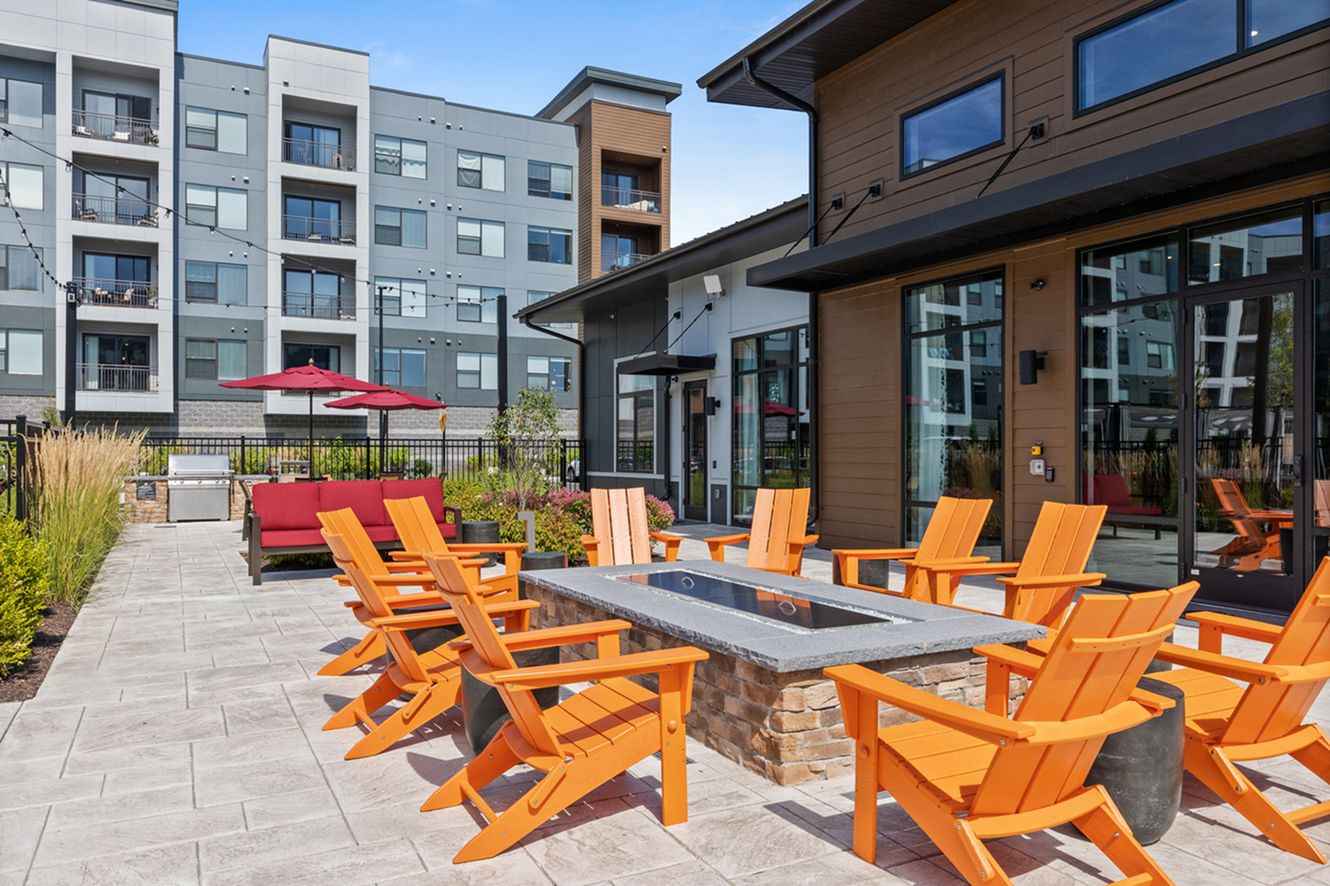 Modern apartment complex with a stylish outdoor seating area featuring orange chairs around a fire pit.