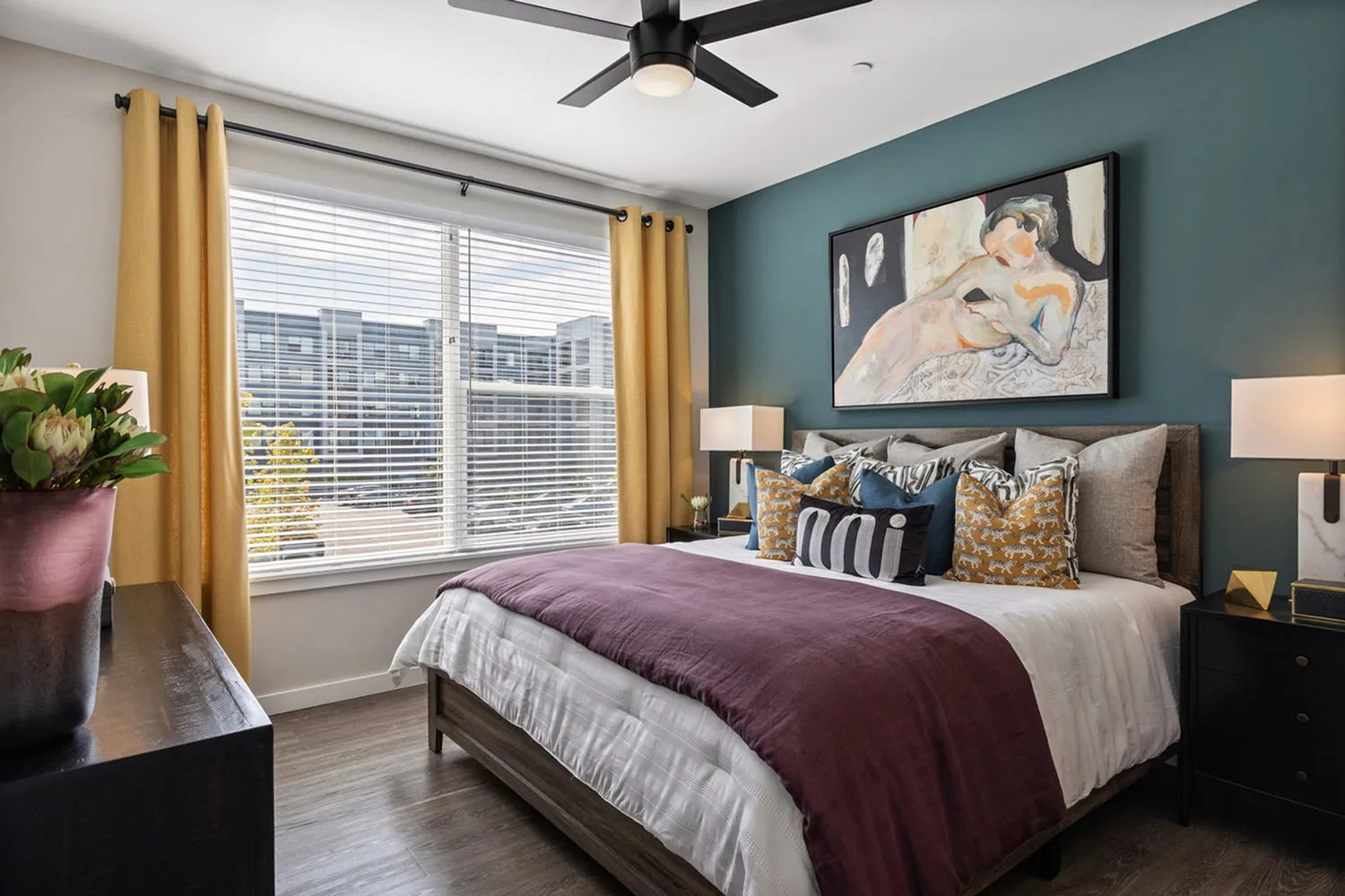 Modern bedroom with stylish decor, featuring a cozy bed, vibrant cushions, and art piece on the wall.