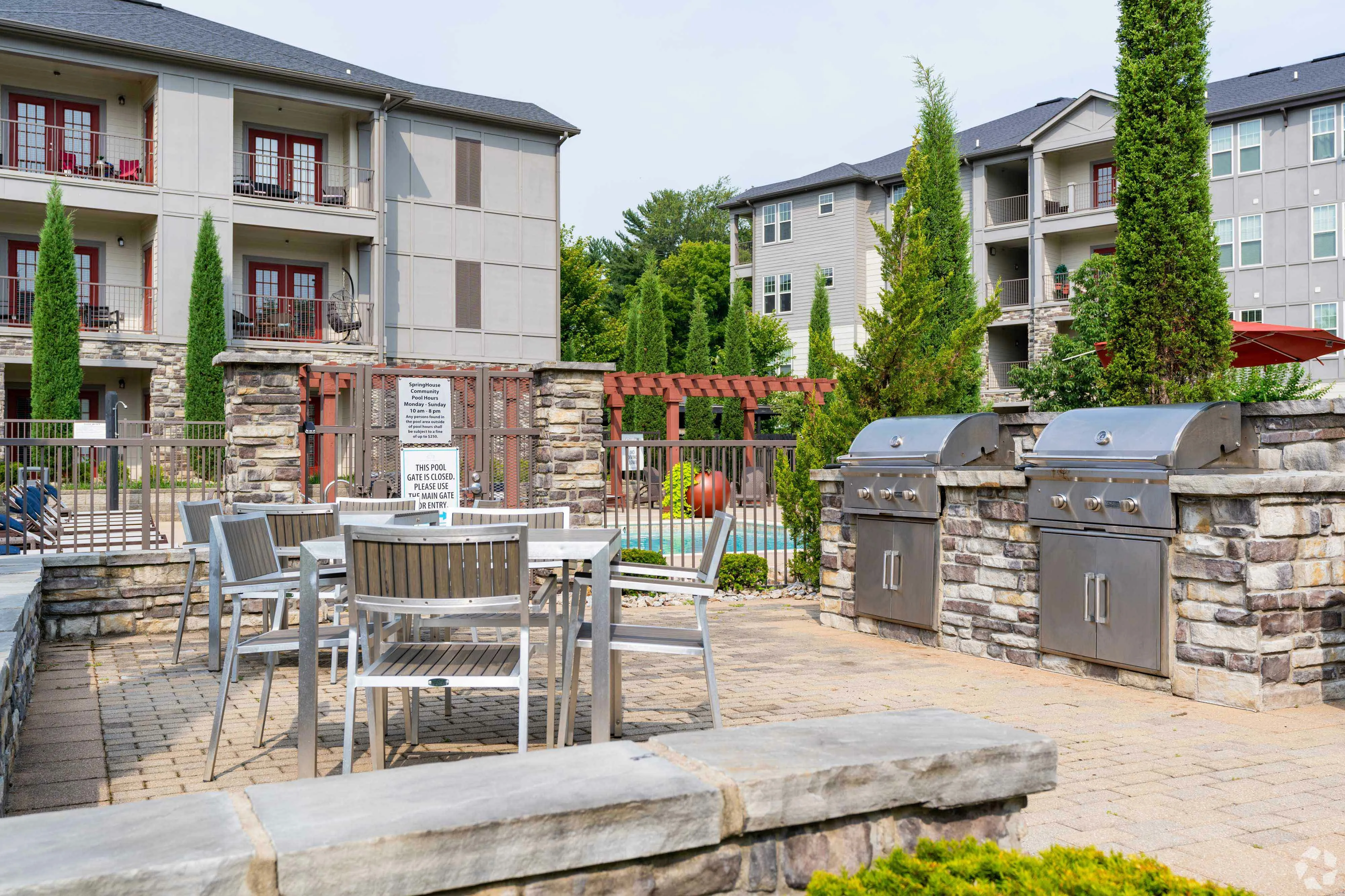 Charming apartment community featuring outdoor dining with grills, lush greenery, and pool.