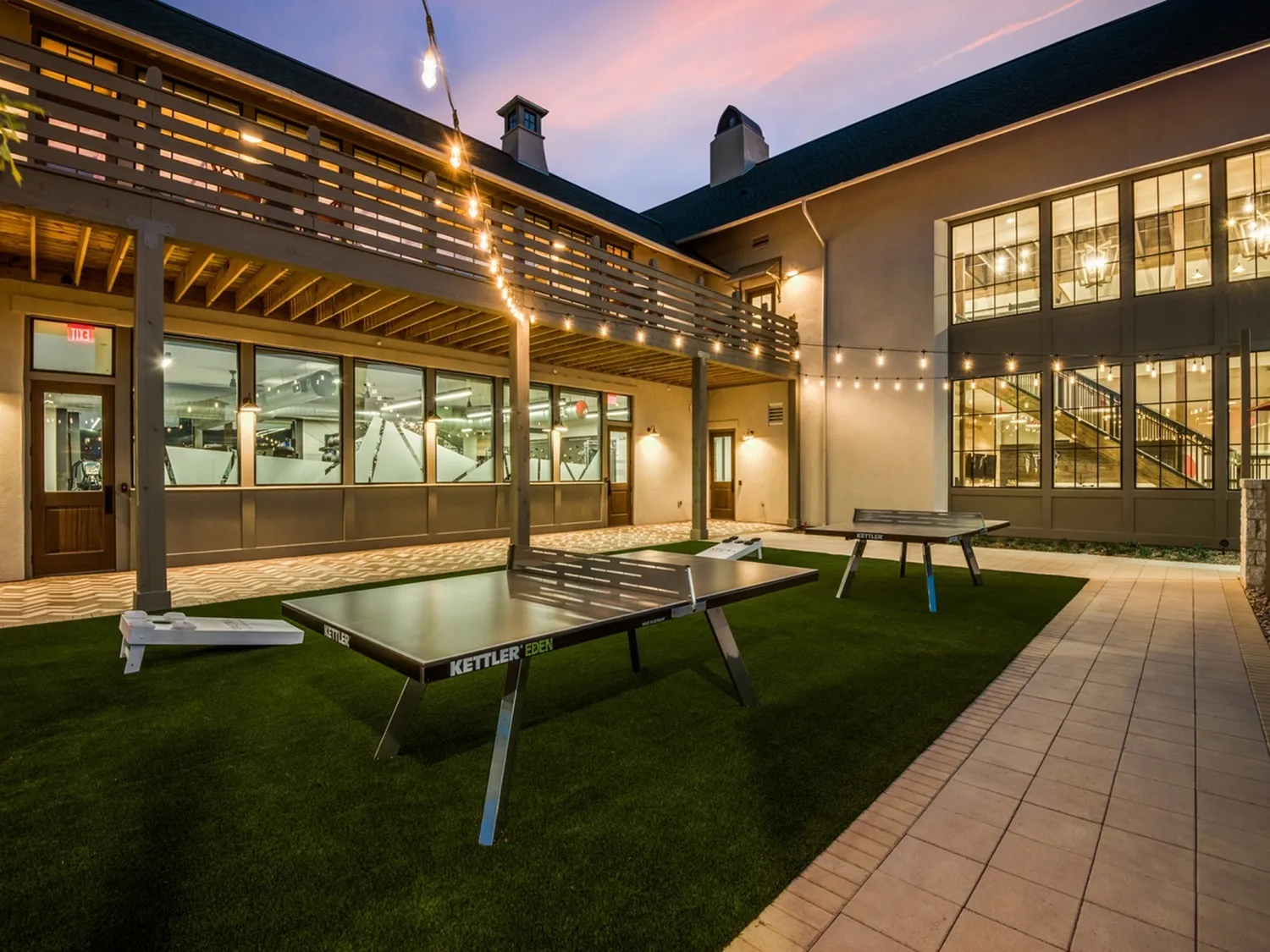 Charming outdoor recreational area with modern table tennis setup, elegant string lights, and a welcoming patio at dusk.