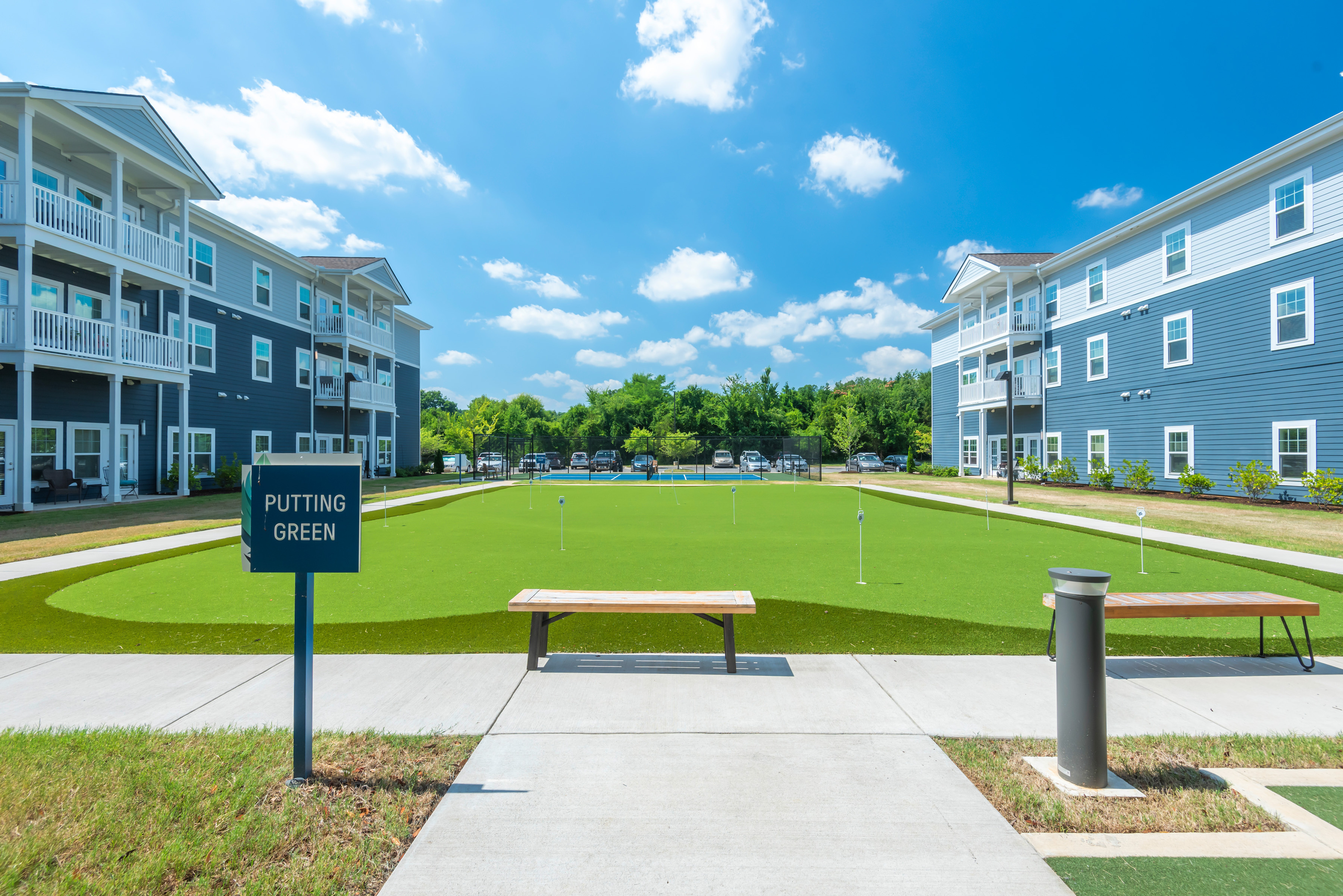 Charming apartment complex featuring modern buildings with private balconies overlooking a pristine putting green under a vibrant blue sky.