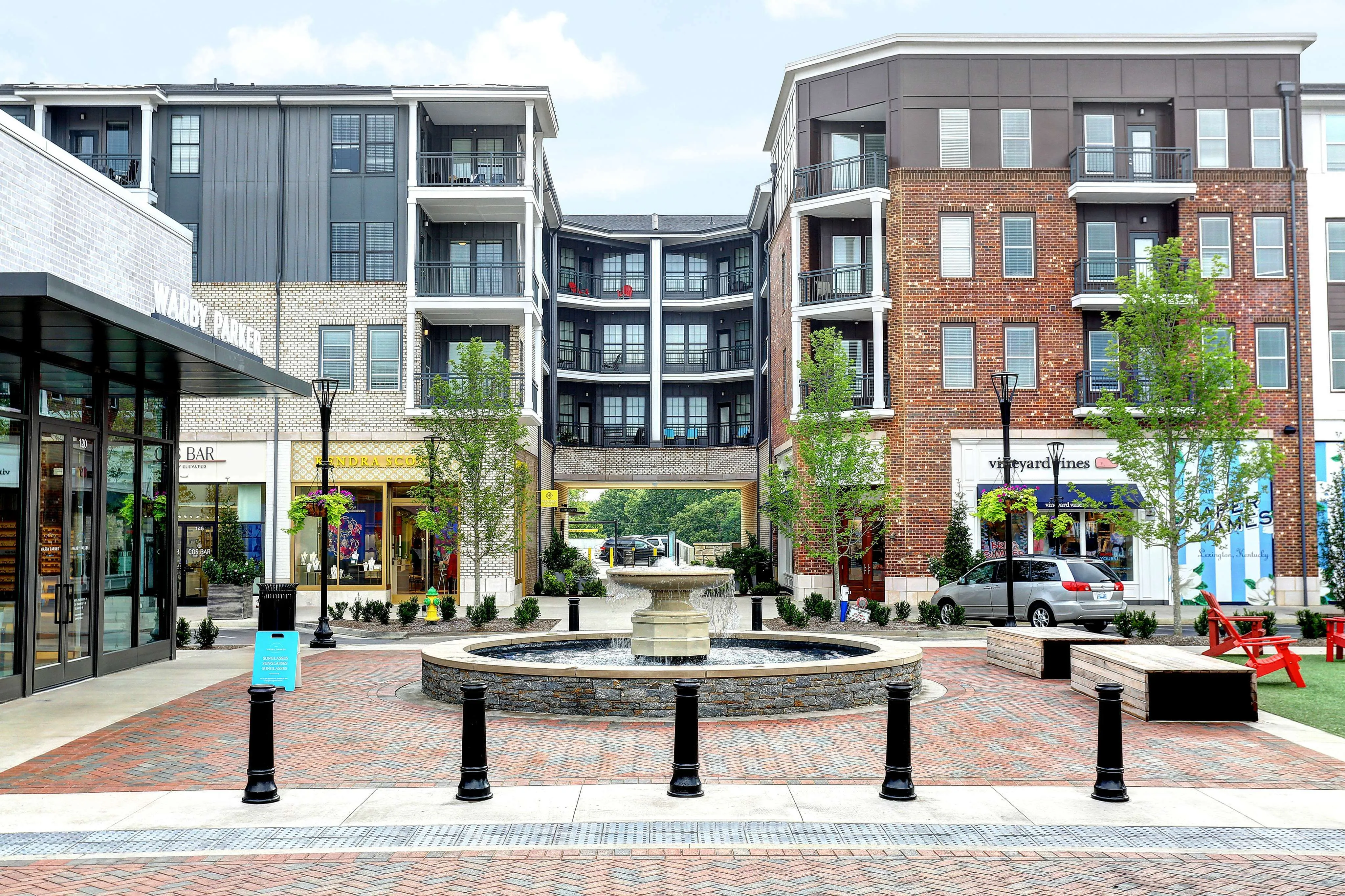 Charming urban apartment complex with modern architecture, vibrant shops, and a central courtyard fountain creating a lively community atmosphere.