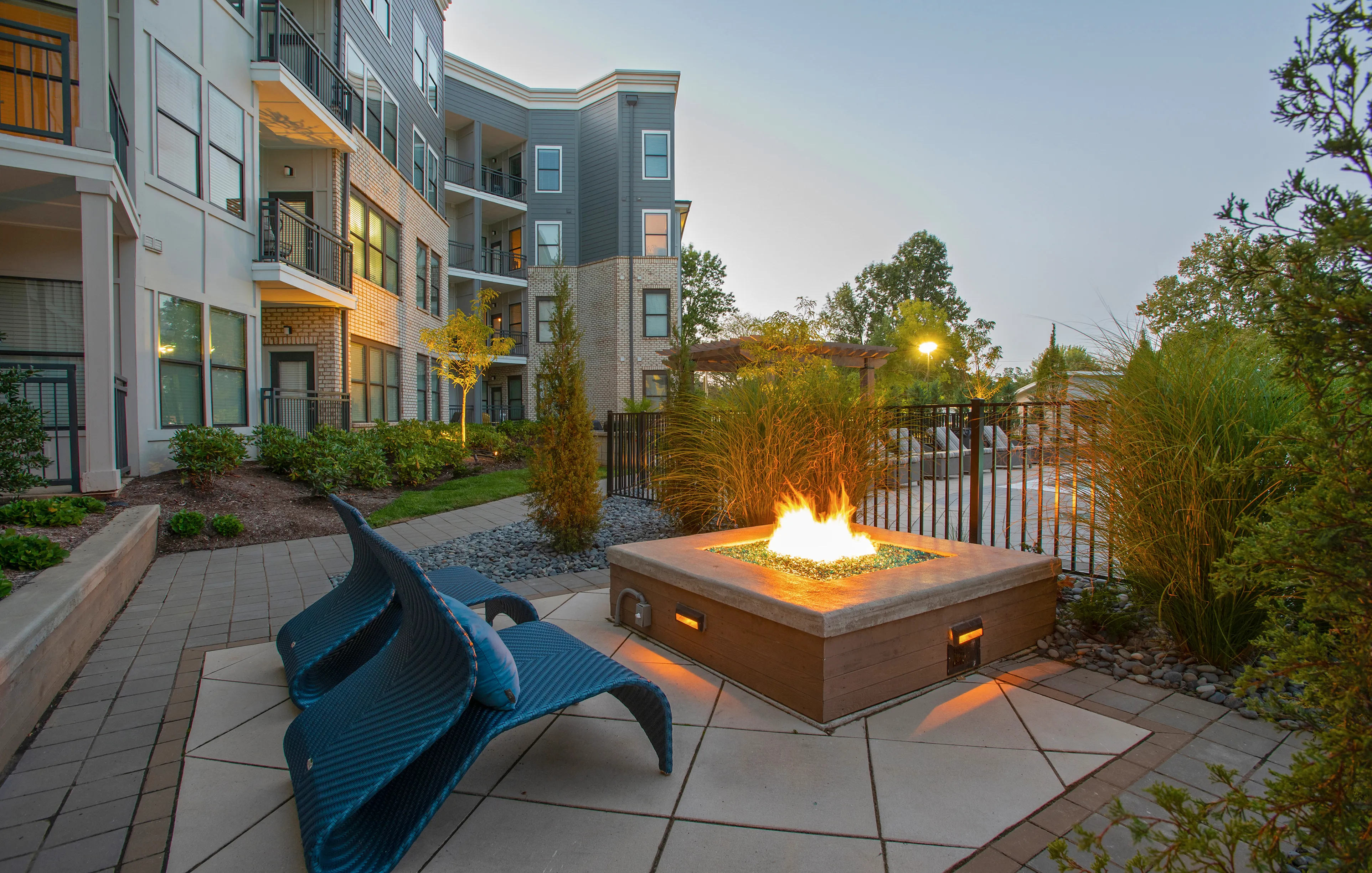 Modern apartment complex with elegant architecture, featuring a cozy outdoor patio with a stylish fire pit and lush greenery.