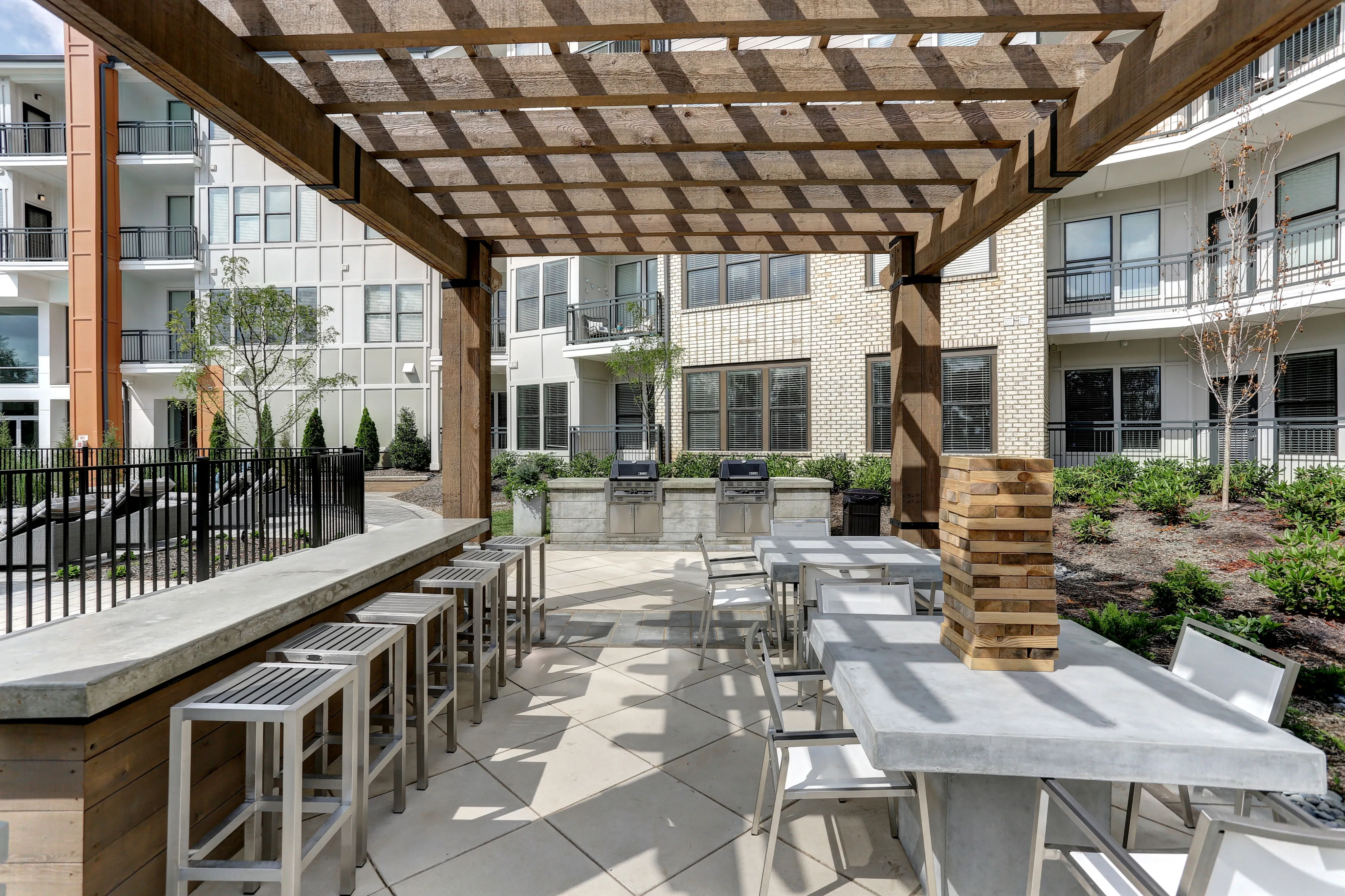 Chic outdoor space featuring elegant dining tables, modern bar seating, and a stylish pergola in a beautifully landscaped apartment complex.