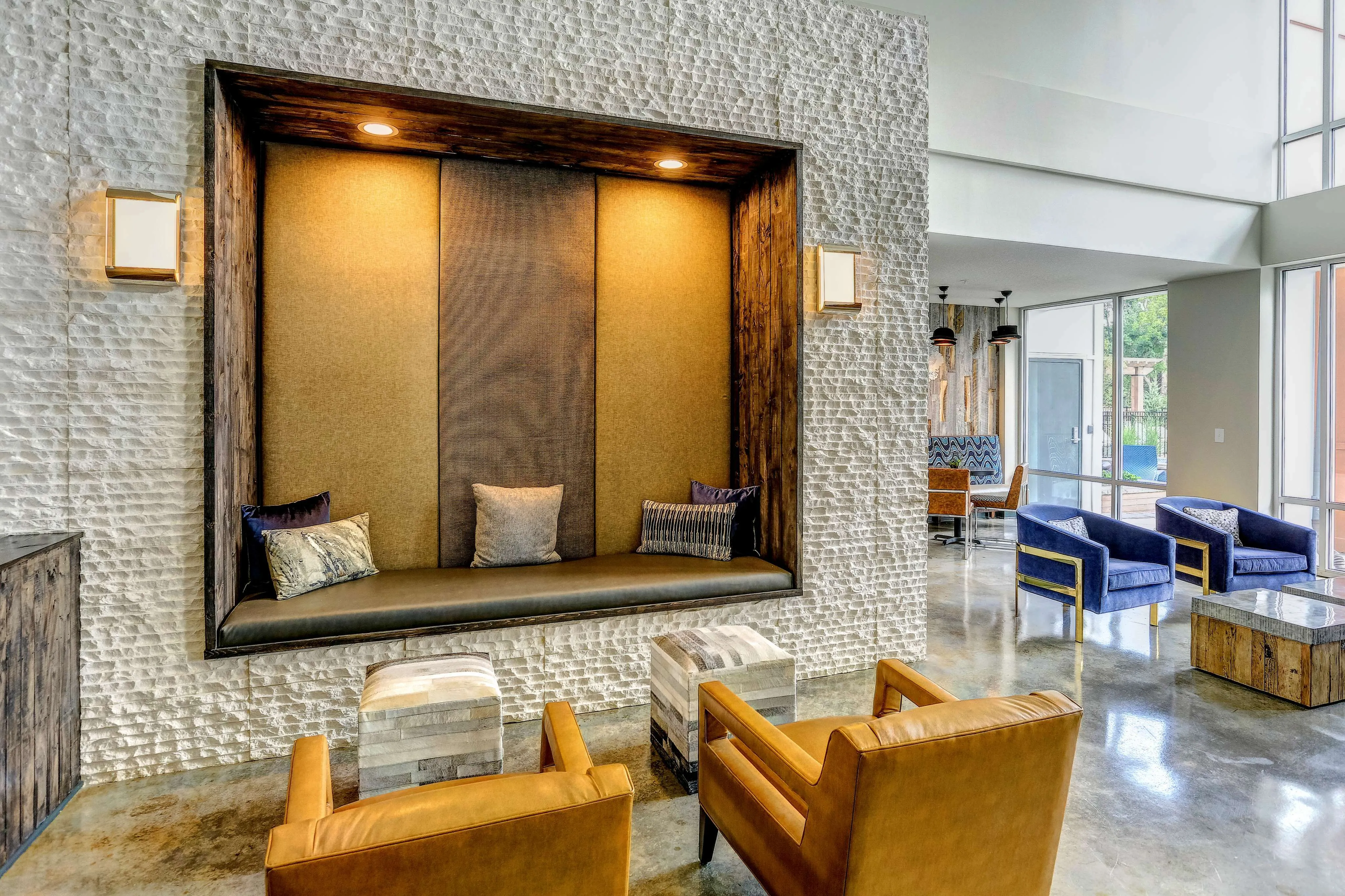 Elegant apartment lounge with modern seating, textured walls, and large windows offering natural light.