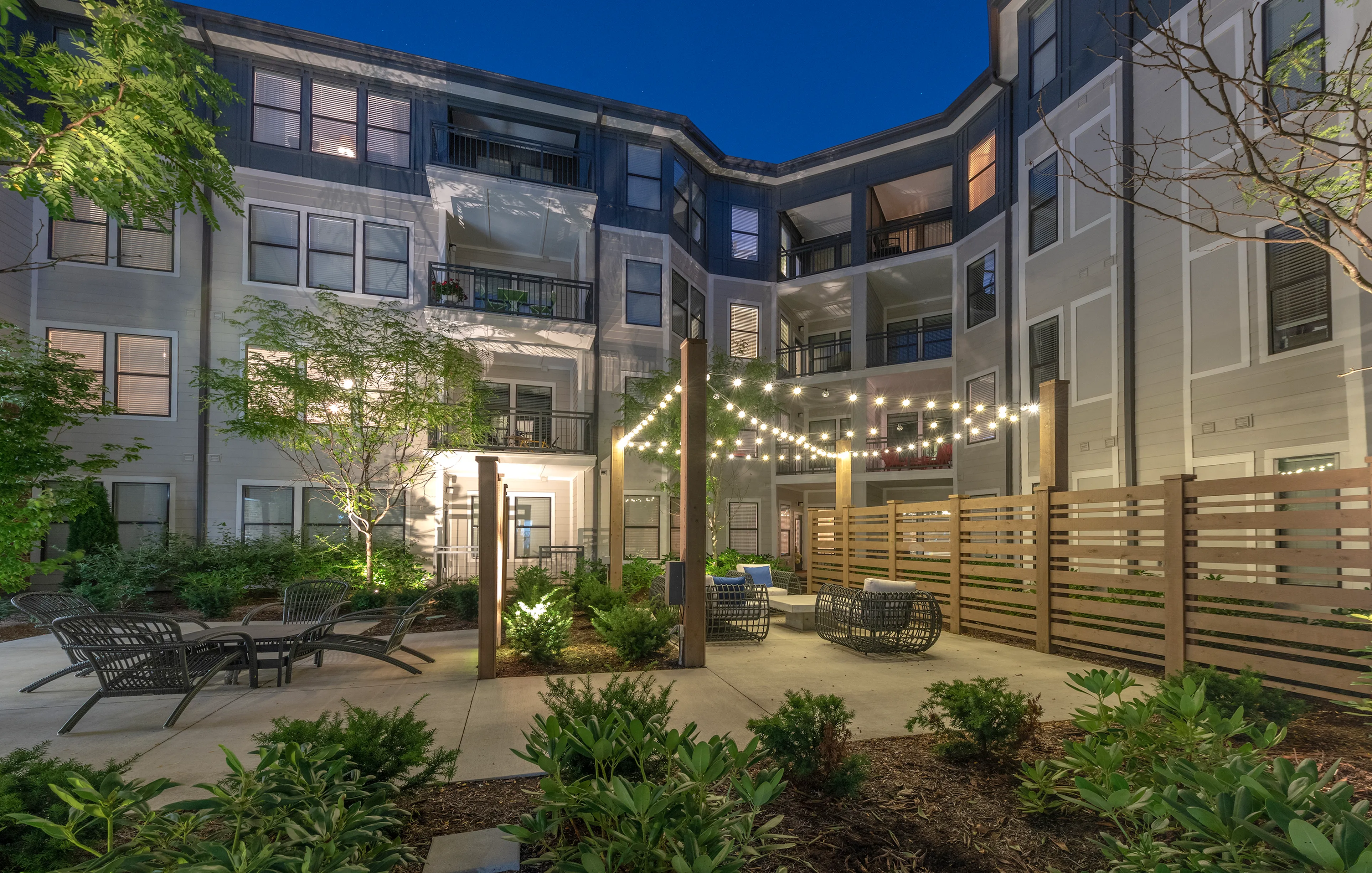 Charming apartment courtyard at night with cozy seating, string lights, and lush greenery creating a serene ambiance.