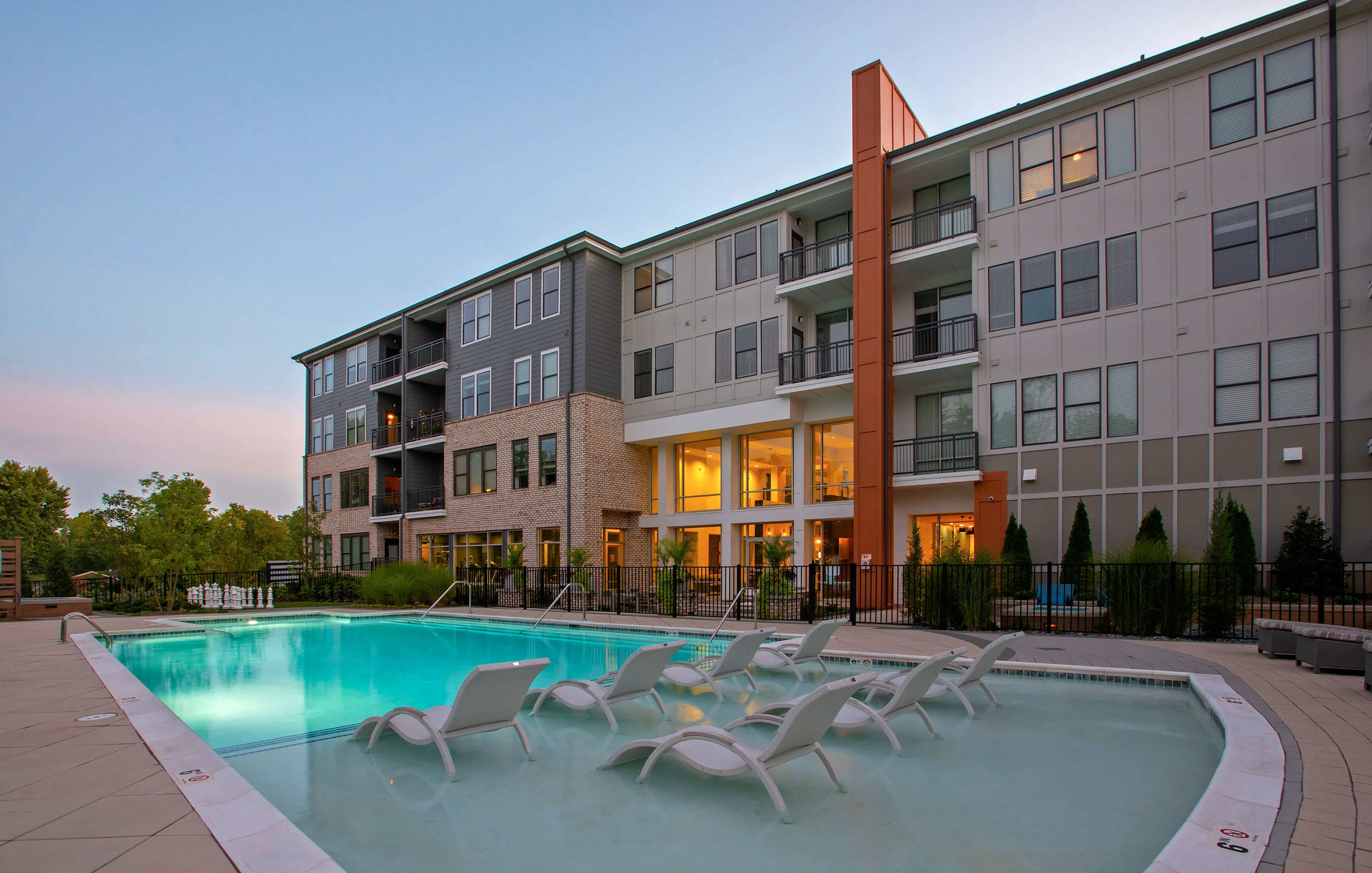 Elegant apartment complex with a resort-style pool, modern design, and inviting outdoor lounge chairs.