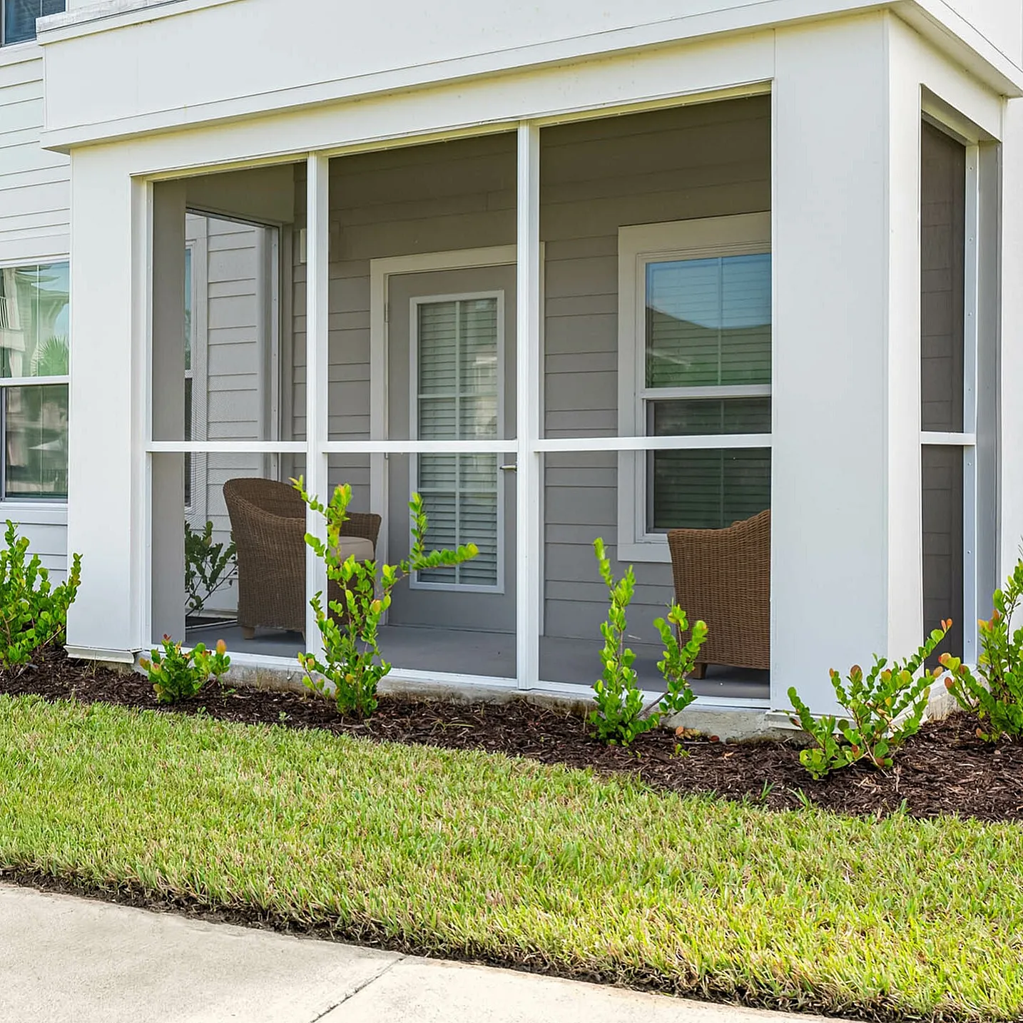 Charming apartment exterior featuring a cozy screened patio, vibrant green lawn, and elegant landscaping.