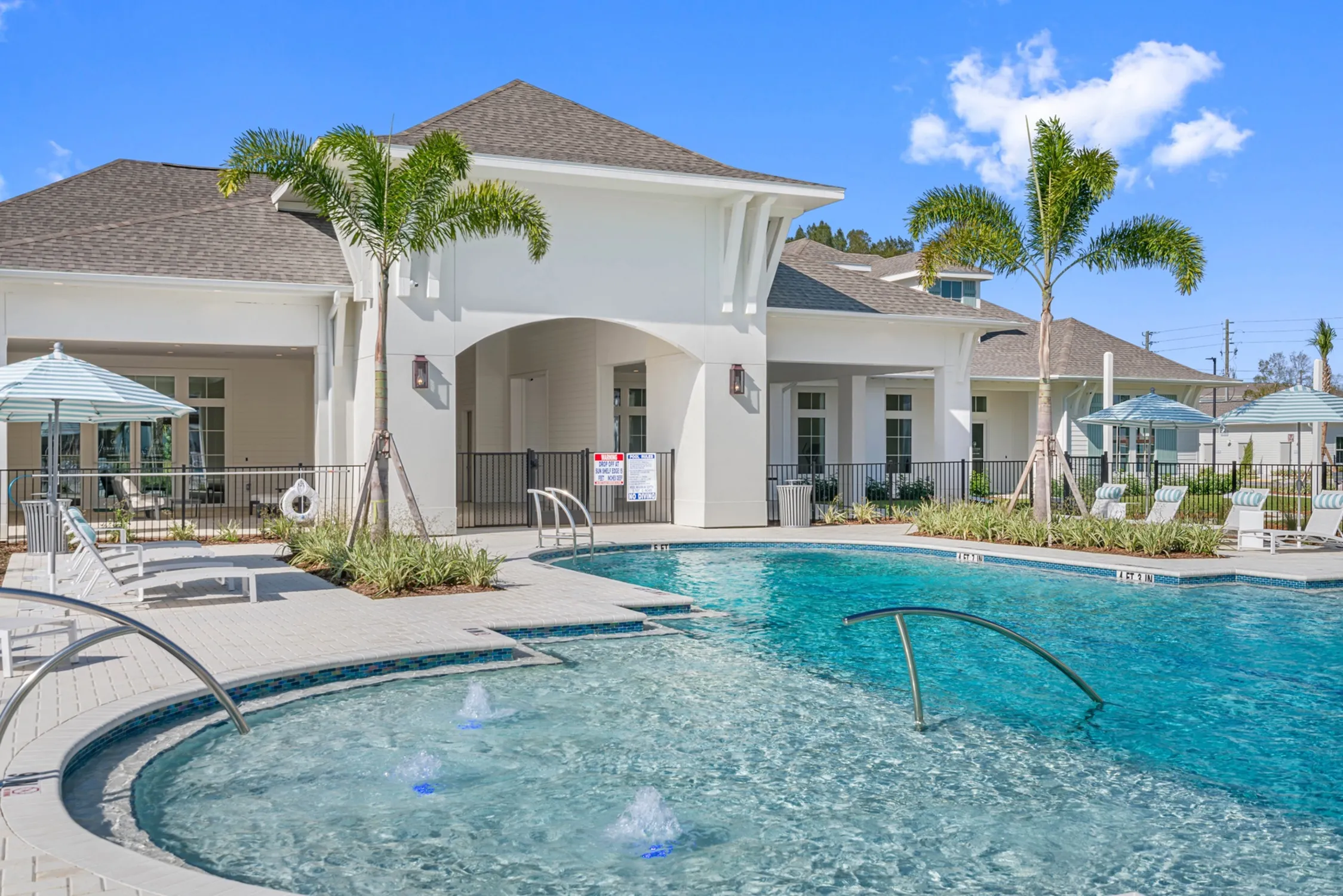 Luxurious resort-style apartment complex with a sparkling pool, sleek white architecture, and elegant palm trees under a bright blue sky.