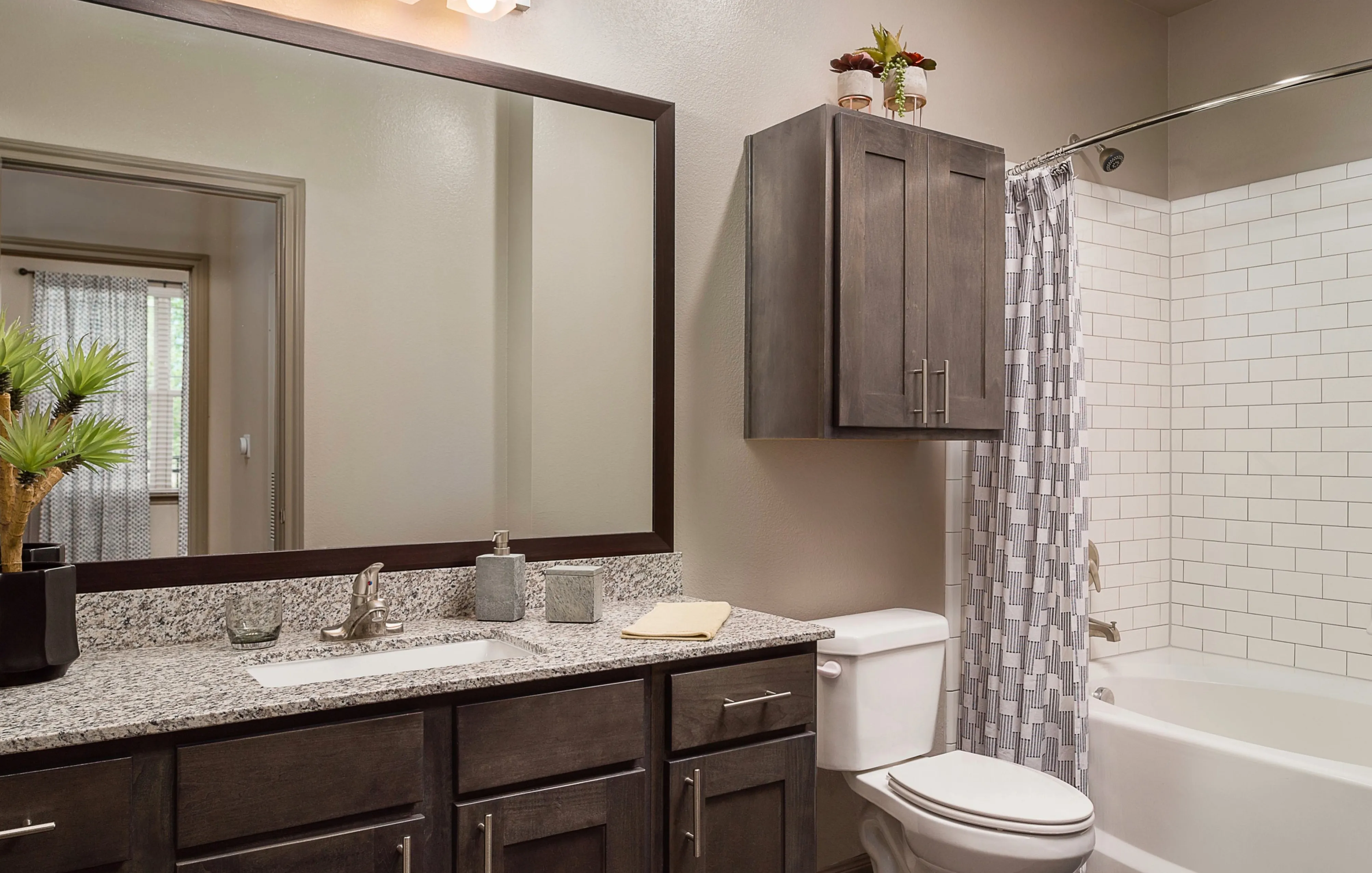 Elegant bathroom featuring a granite countertop, chic dark cabinetry, and a stylish tiled shower area.
