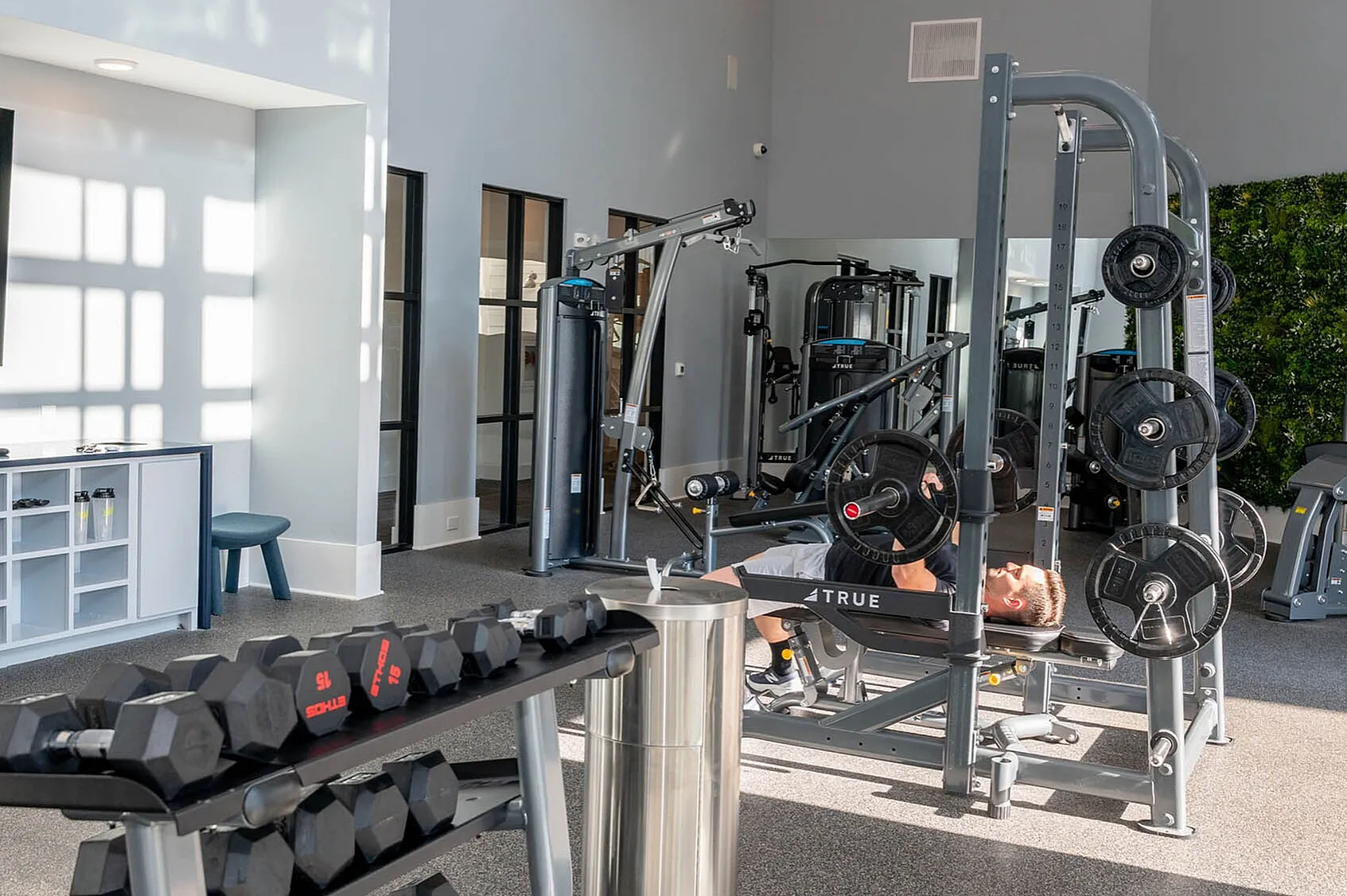 Modern gym with state-of-the-art equipment including weights and a bench press, complemented by natural light and sleek interior design.