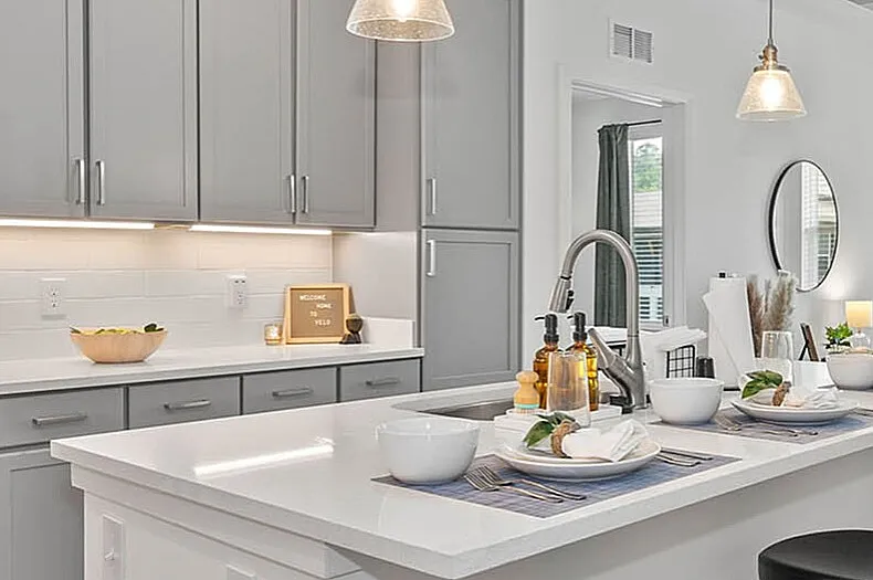 Modern open-concept kitchen with sleek gray cabinets and elegant island, seamlessly flowing into a bright, stylish living area with floor-to-ceiling windows.