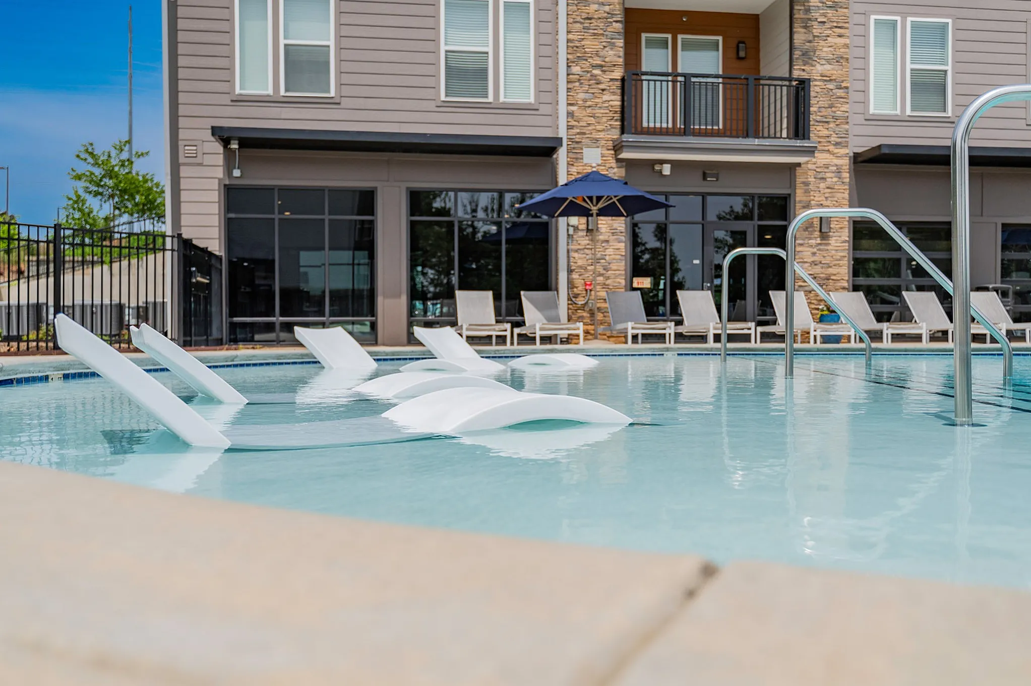 Luxurious apartment community pool with stylish submerged loungers and chic stone facade.