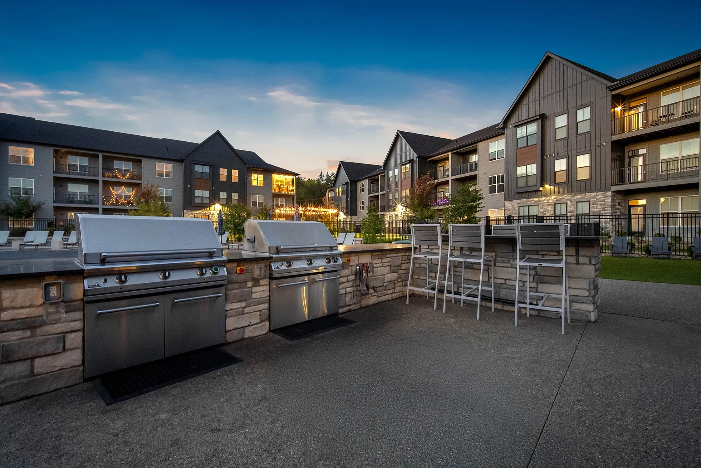 Charming apartment complex with elegant stone outdoor grilling area and inviting evening lighting, perfect for relaxation and entertainment.