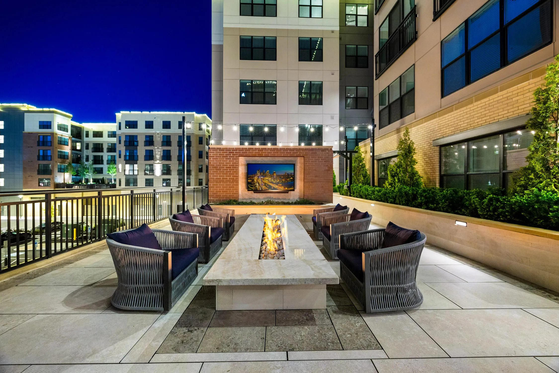 Chic apartment patio with cozy seating around a modern fire pit, evening lights enhancing the stylish urban ambiance.