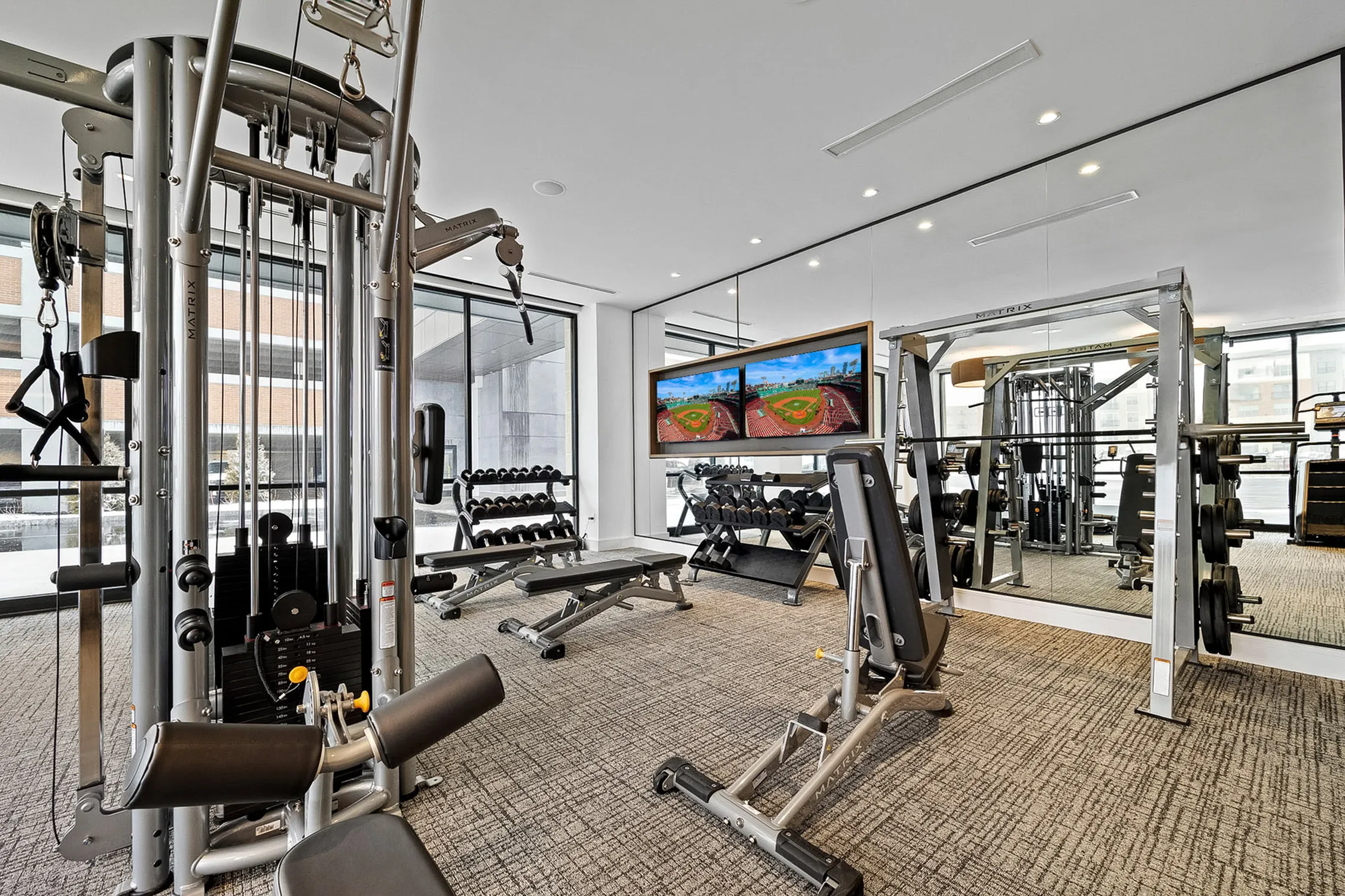 Modern fitness center with high-tech gym equipment, weight racks, and mirrored walls in a well-lit, spacious area.