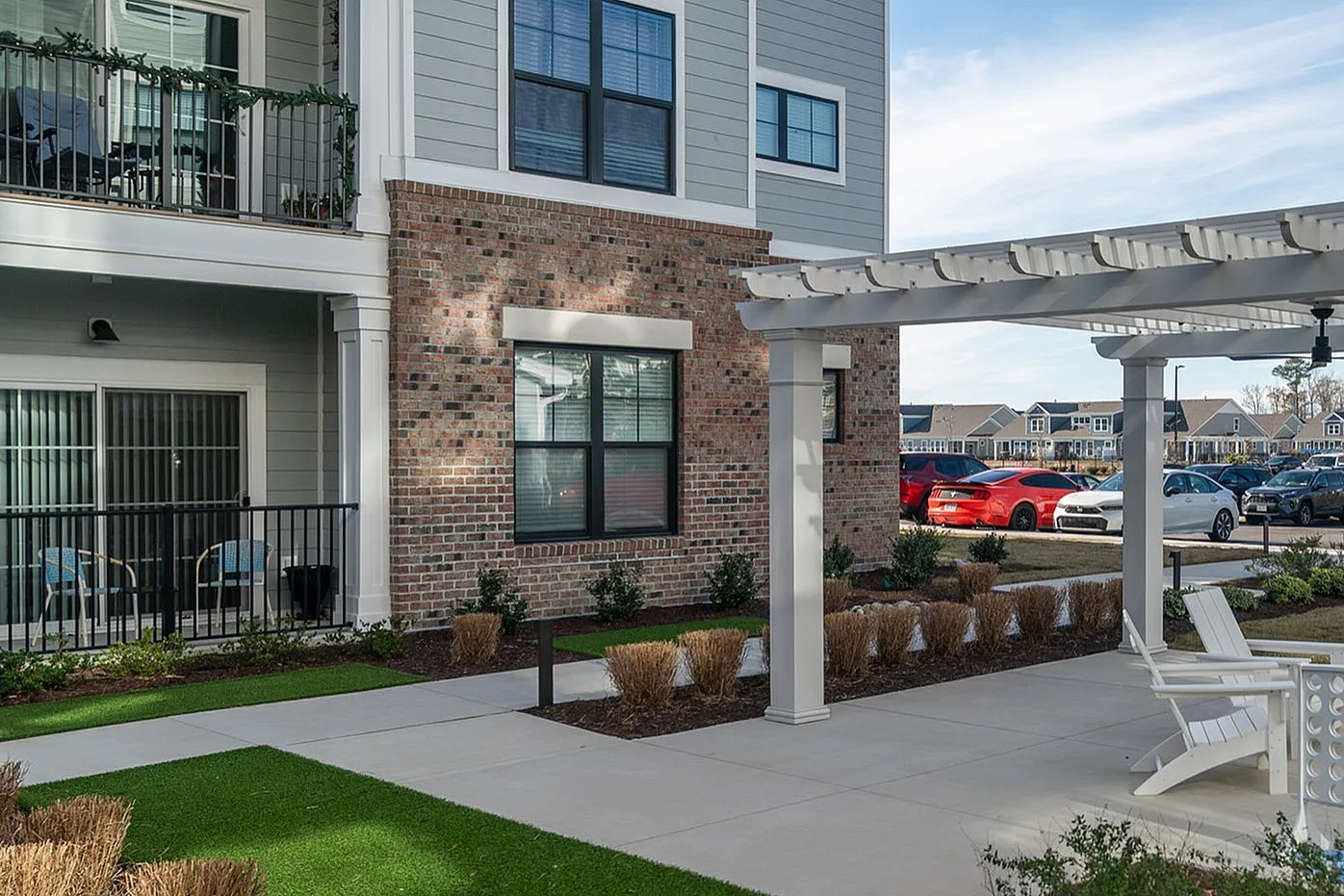 Modern apartment complex featuring a charming outdoor pergola with seating, surrounded by lush greenery and well-manicured landscapes.