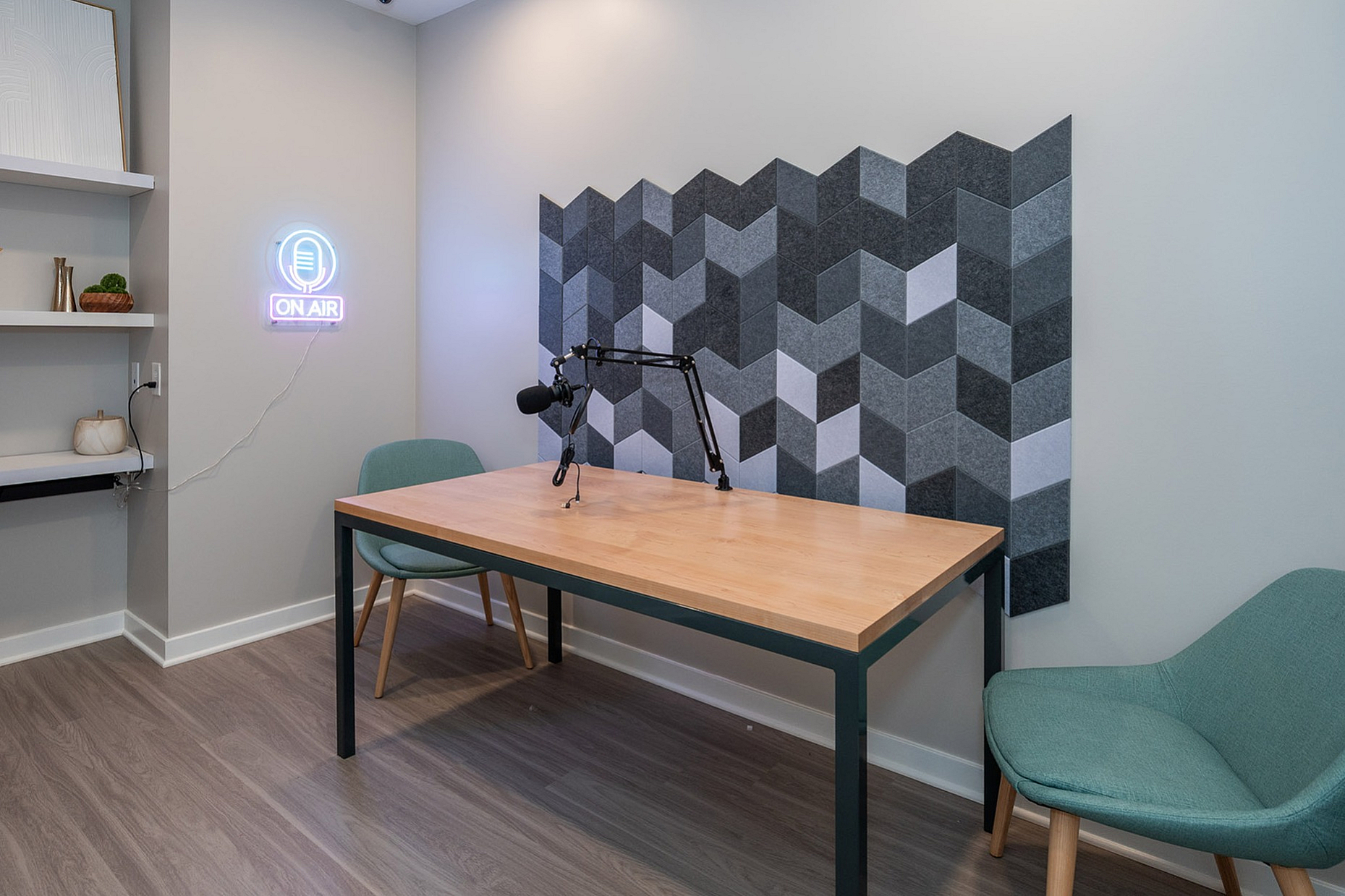 Contemporary home studio with chic geometric wall design, cozy seating, and \'On Air\' neon sign for a stylish and professional workspace.