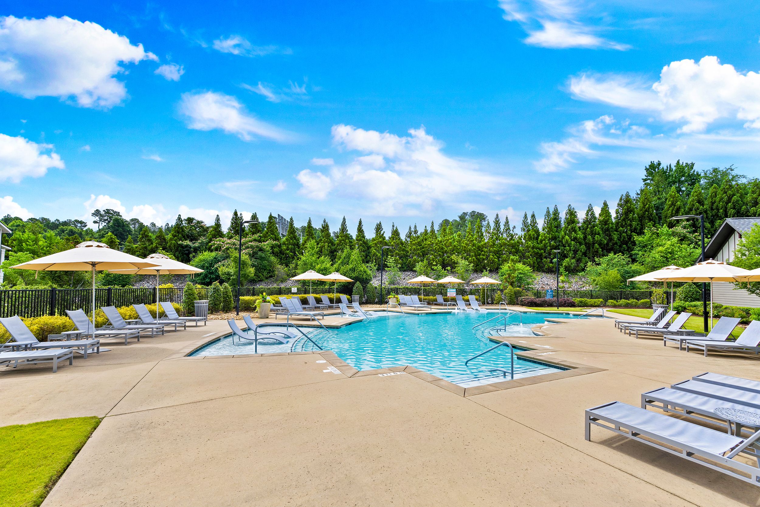 Pristine outdoor pool area with elegant lounge chairs and umbrellas, surrounded by lush greenery under a clear blue sky.
