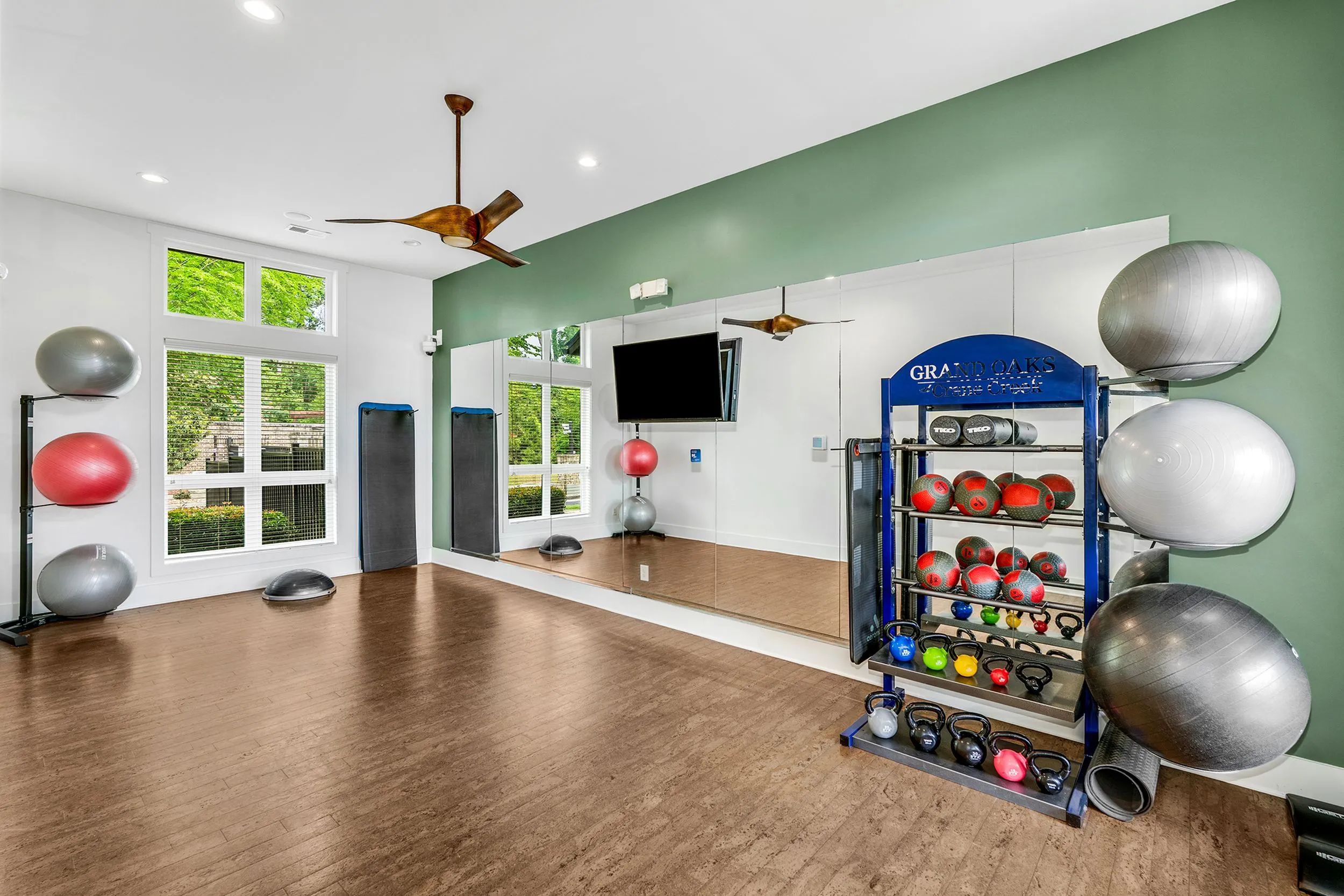 Bright and modern fitness studio with mirrored wall, exercise balls, weights rack, and wooden flooring—ideal for dynamic workouts.