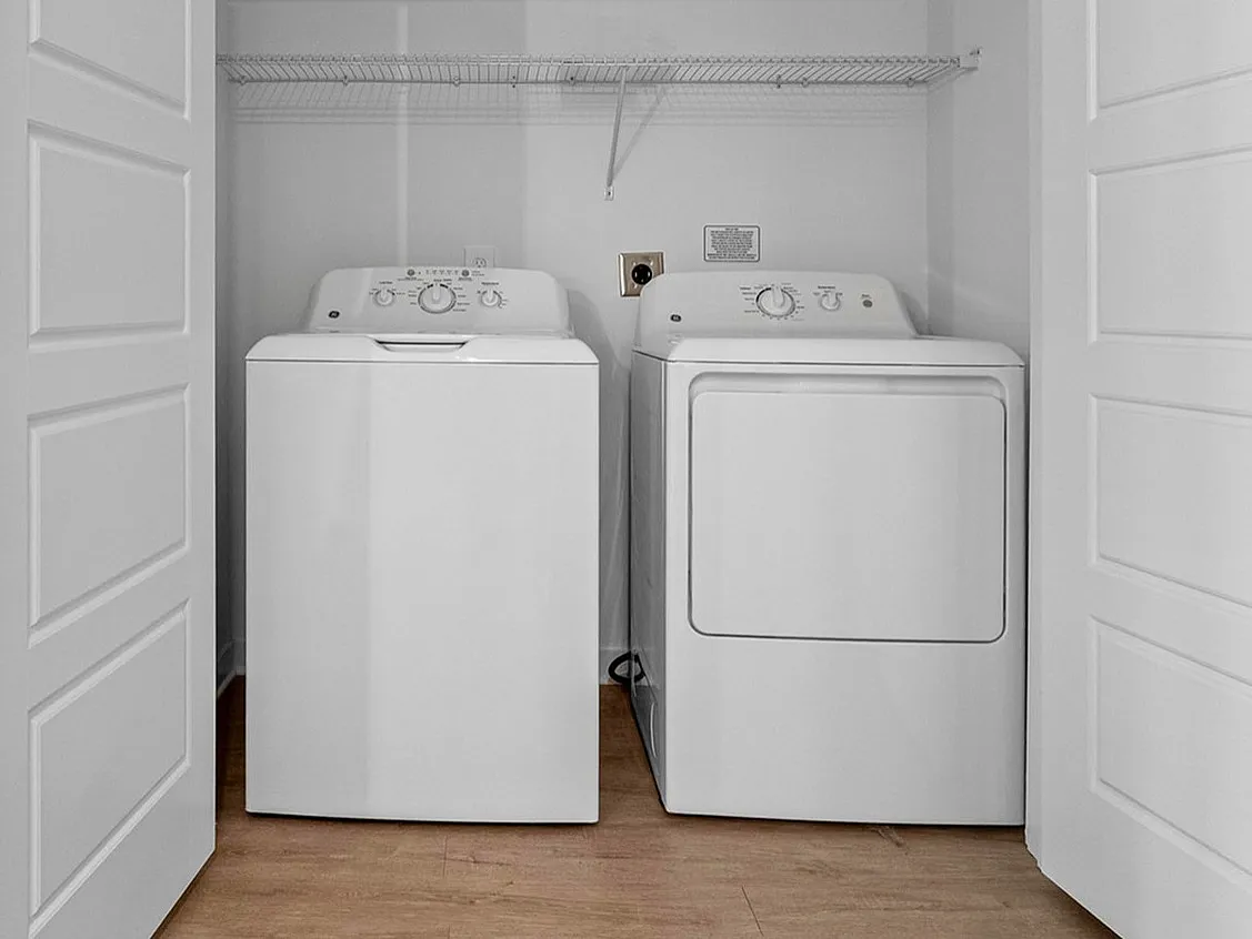 Modern apartment laundry area with sleek washer and dryer, offering convenience and style with white paneled closet doors and wood flooring.