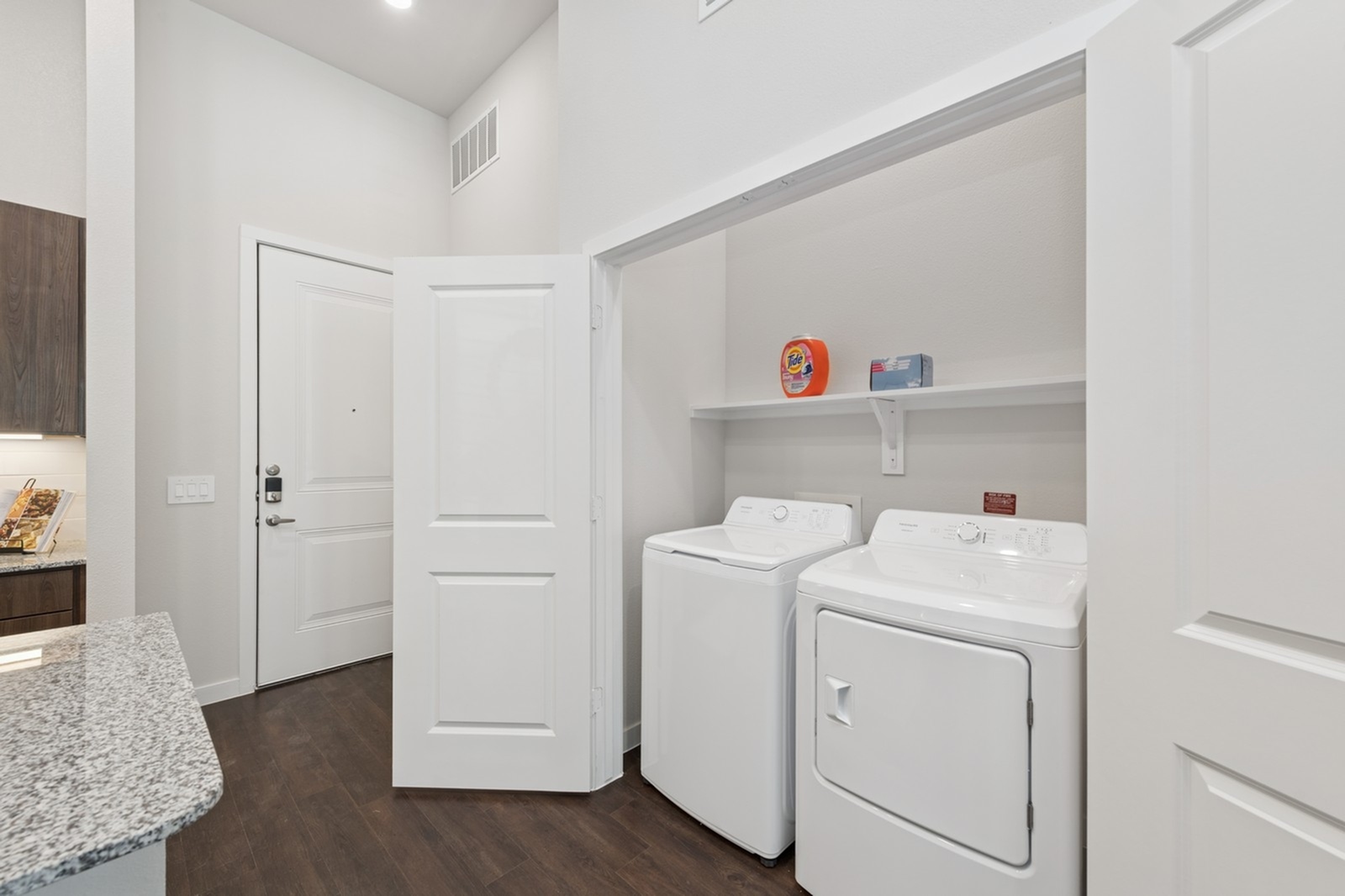 Modern apartment entry with convenient in-unit laundry featuring energy-efficient washer and dryer, adjacent to sleek granite kitchen counter.