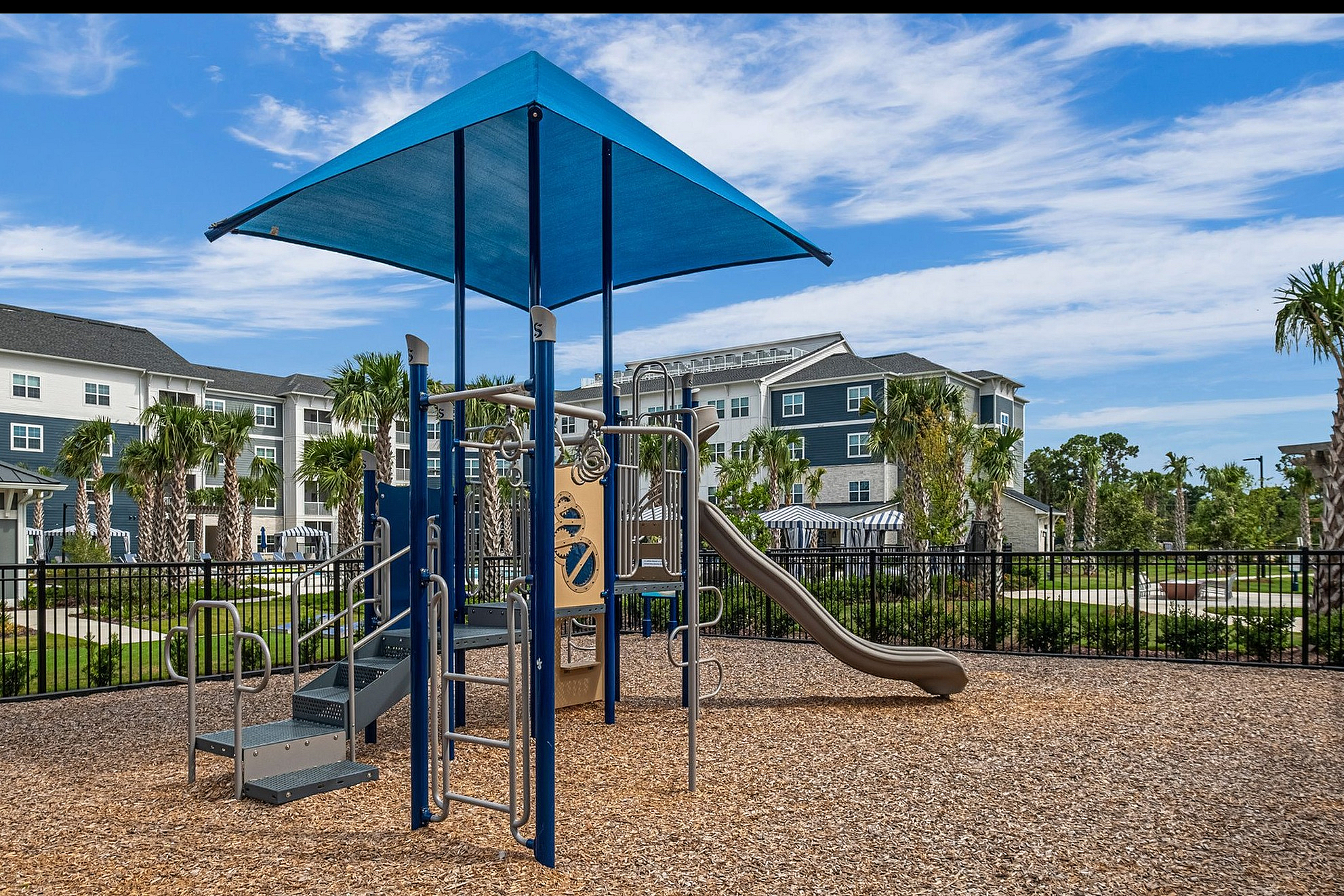 Inviting outdoor playground set against a backdrop of modern apartments and lush palm trees, perfect for family-friendly living.