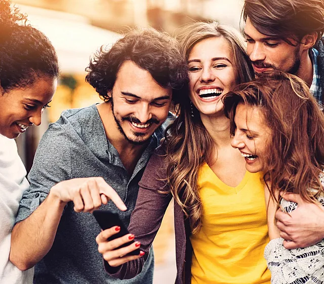 Joyful group of friends smiling and looking at a smartphone outdoors.