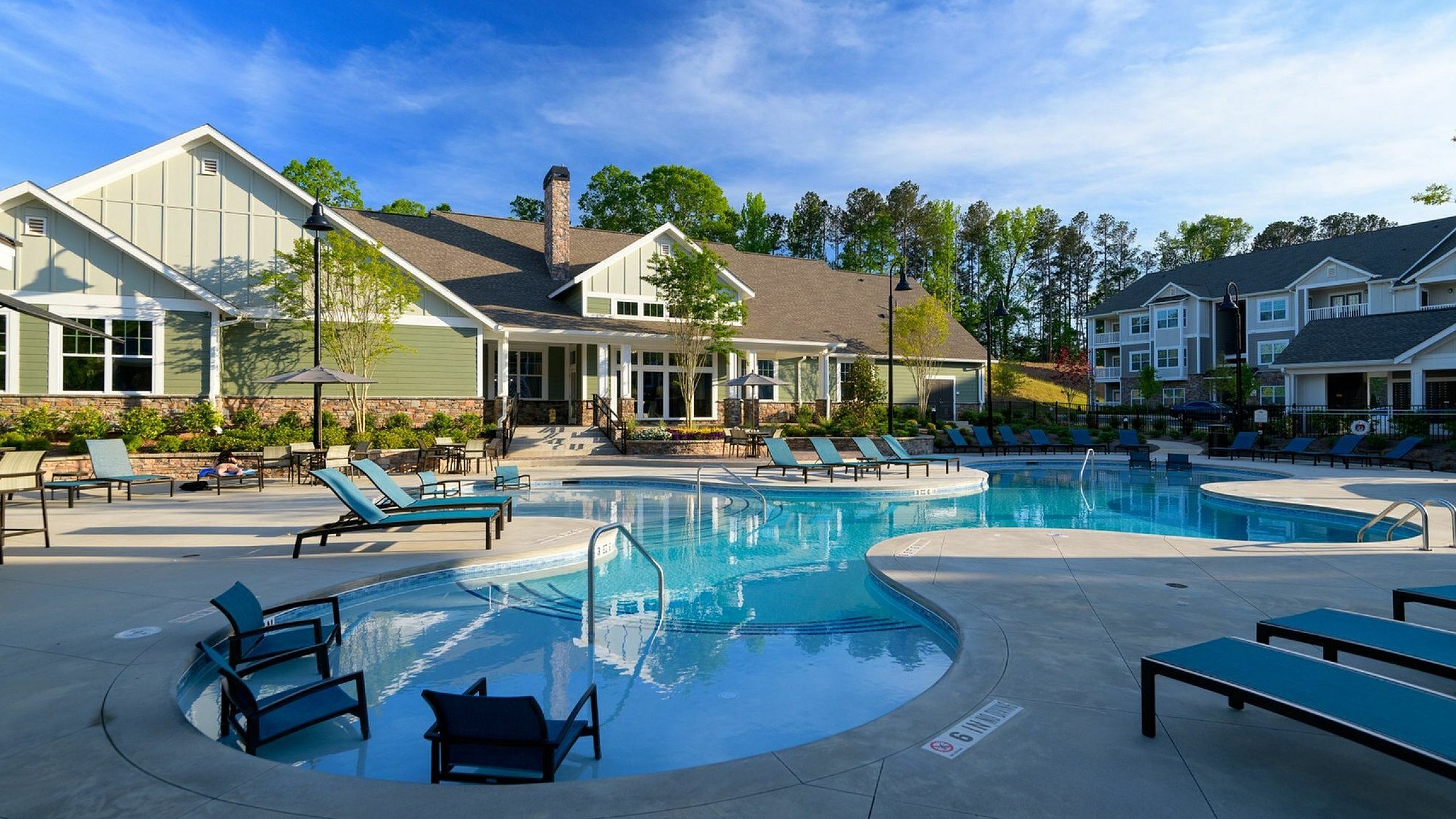 Stunning outdoor pool area with sun loungers and modern apartment buildings under a clear blue sky.
