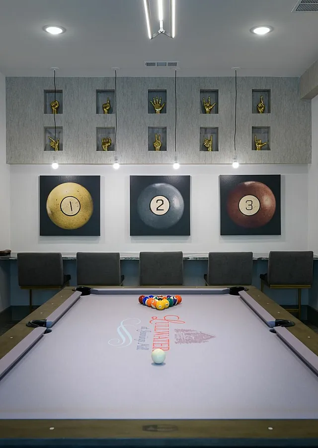Contemporary game room with a sleek pool table, artistic wall decor with numbers and hand sculptures, and ambient lighting.