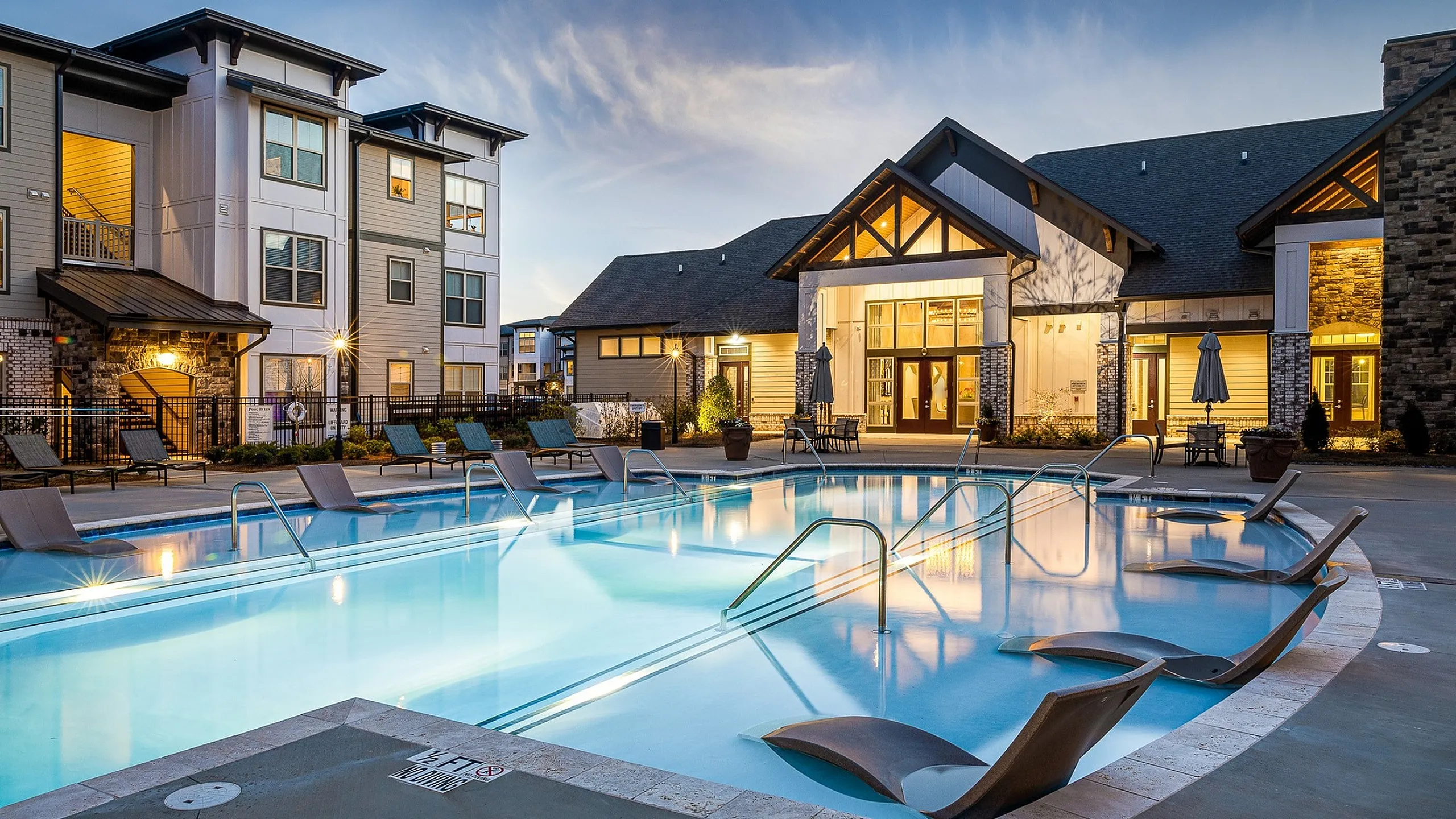 Charming evening poolside view at a luxury apartment complex with elegant architecture and inviting loungers.